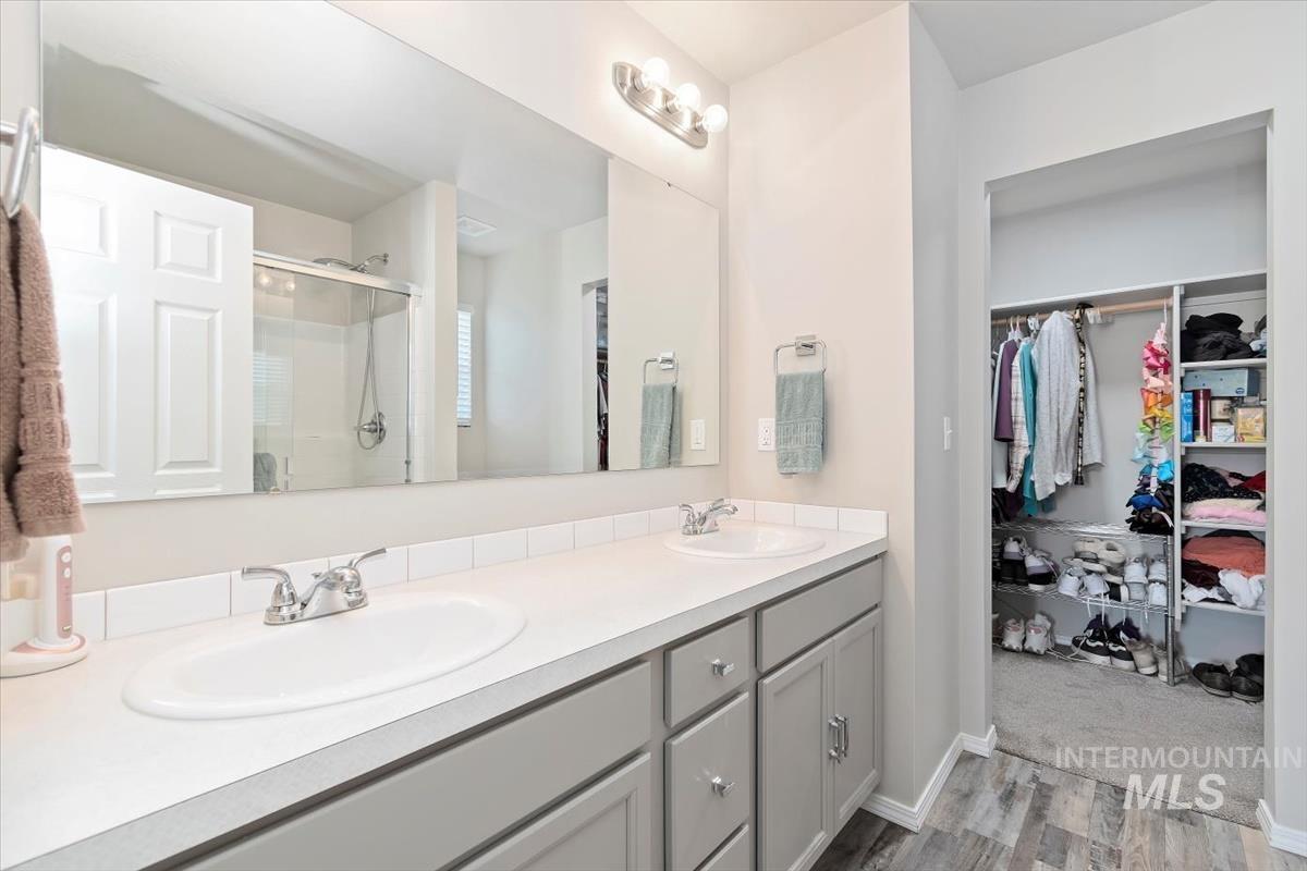 Bathroom featuring double vanity, a shower stall, light wood-type flooring, and a spacious closet