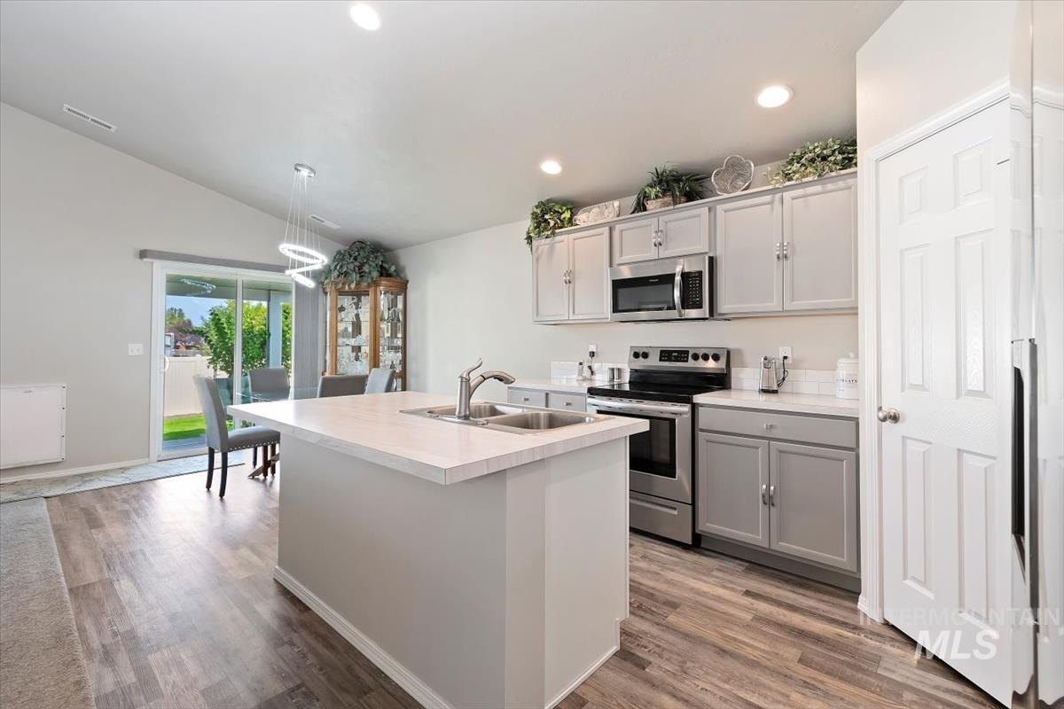 Kitchen with gray cabinetry, light countertops, stainless steel appliances, a kitchen island with sink, and recessed lighting