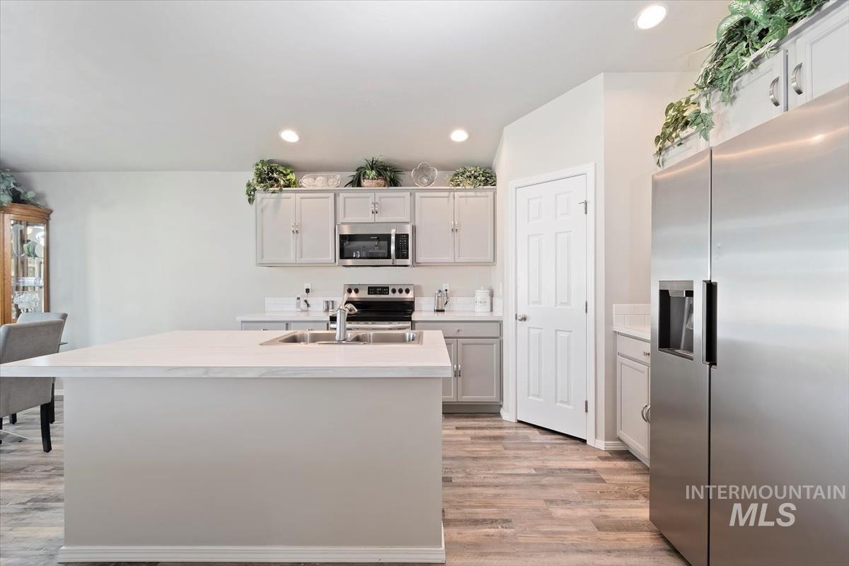 Kitchen featuring stainless steel appliances, a center island with sink, light countertops, light wood finished floors, and recessed lighting