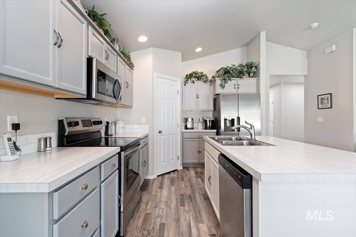 Kitchen featuring appliances with stainless steel finishes, light countertops, dark wood-style flooring, recessed lighting, and an island with sink