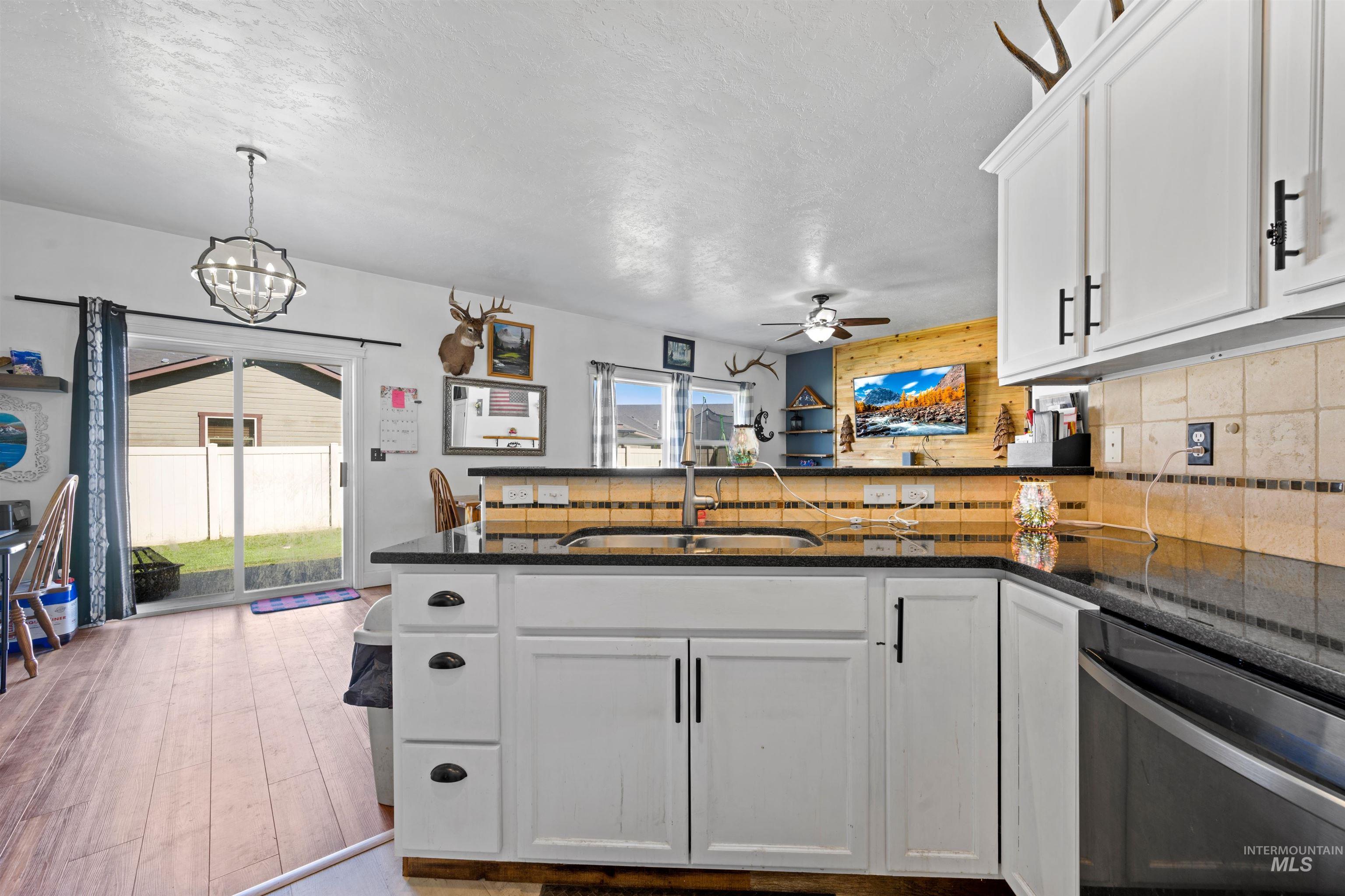 Kitchen with white cabinets, a peninsula, tasteful backsplash, dishwasher, and a textured ceiling