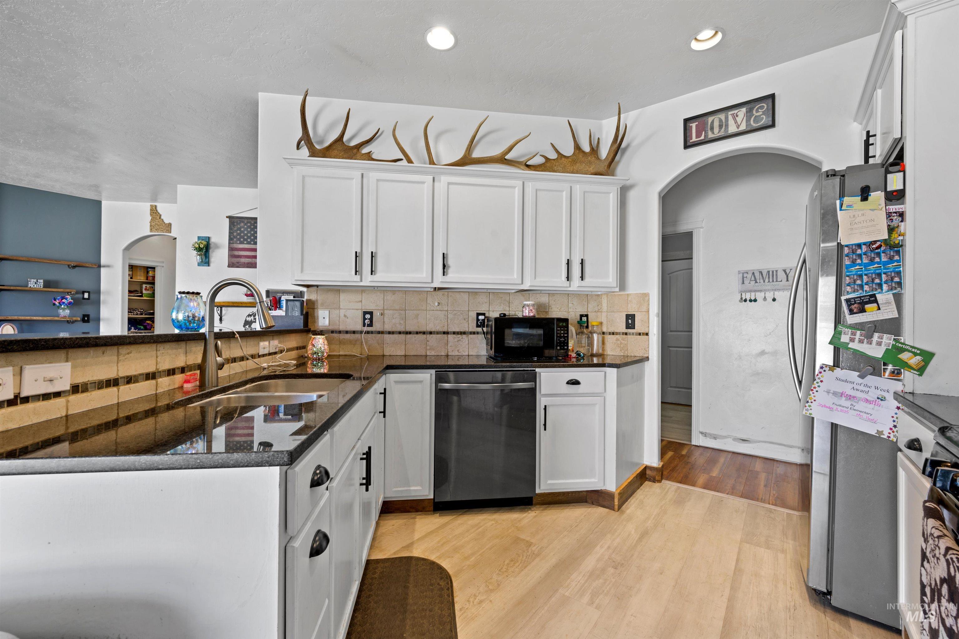 Kitchen with arched walkways, white cabinetry, light wood finished floors, black appliances, and recessed lighting