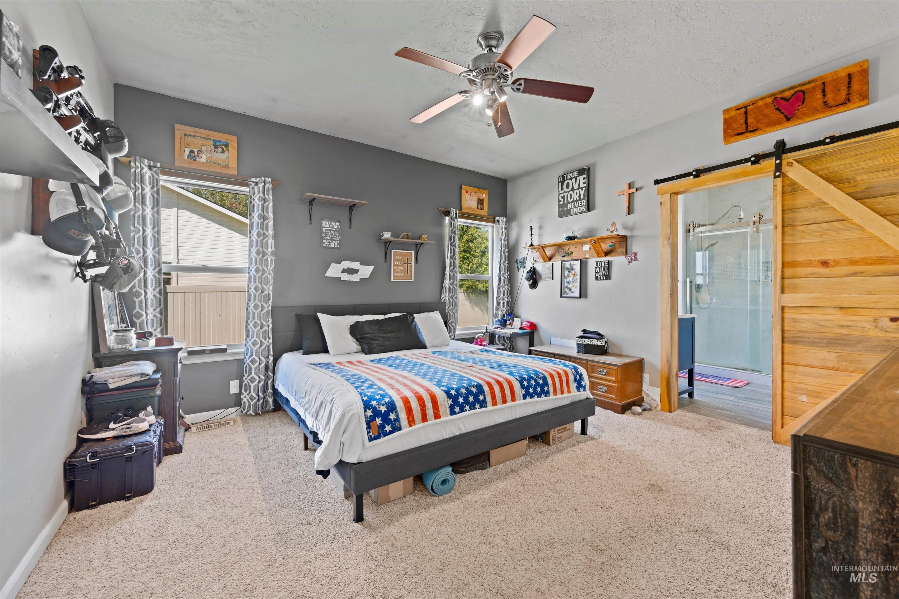 Bedroom with a barn door, light colored carpet, multiple windows, and a textured ceiling