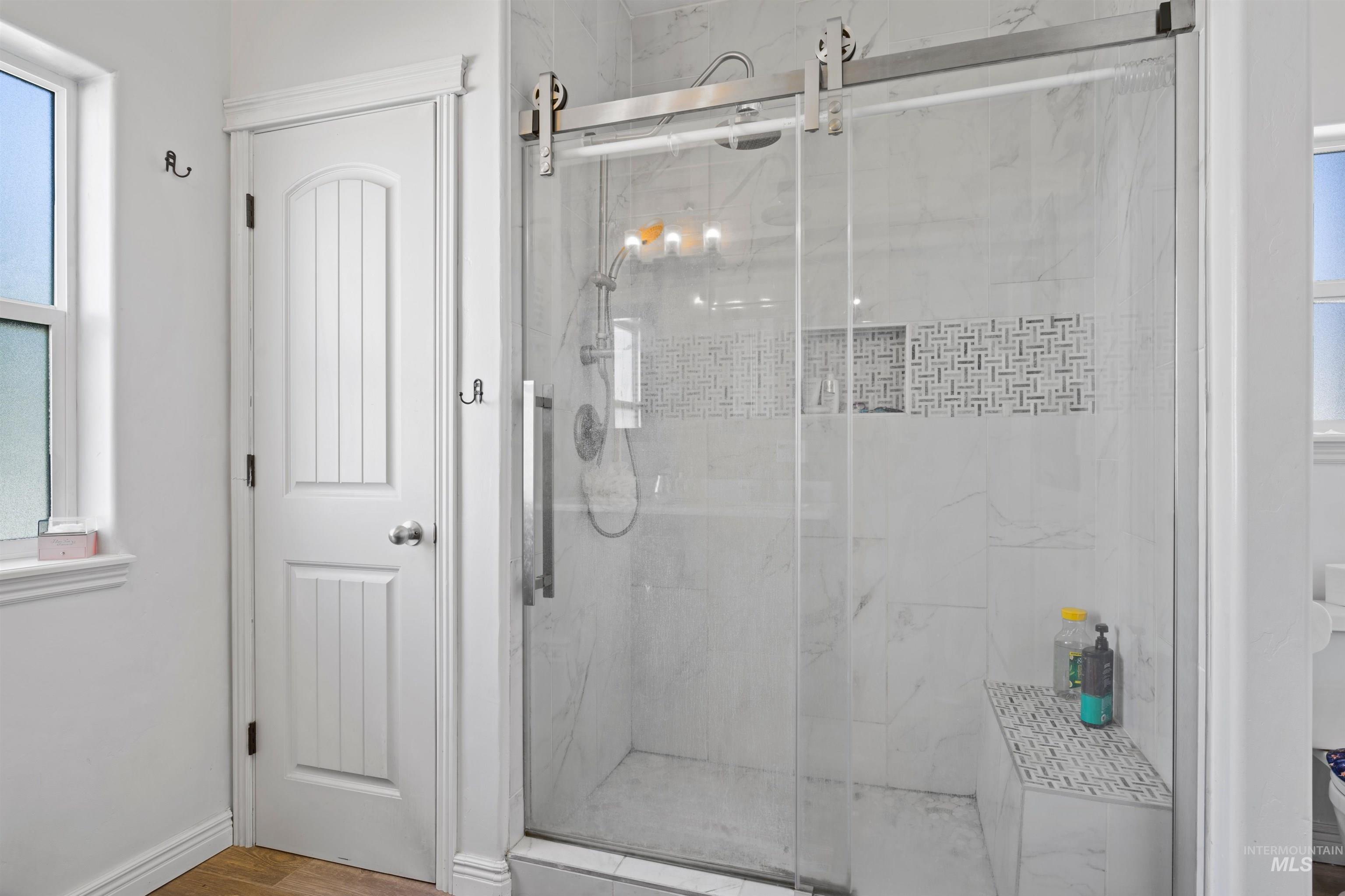 Bathroom with healthy amount of natural light, a marble finish shower, and wood finished floors
