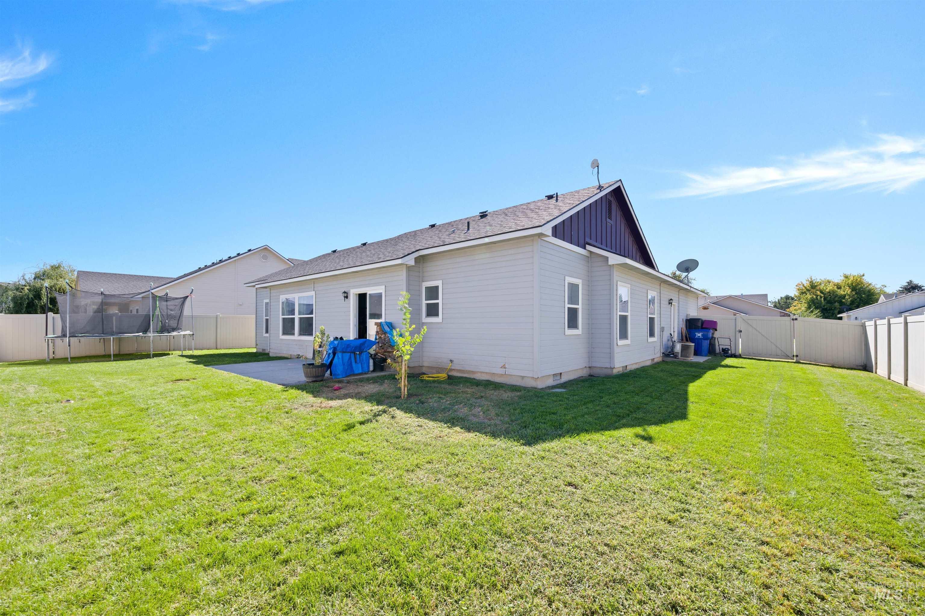 Rear view of property with a trampoline, a fenced backyard, a gate, a patio area, and roof with shingles