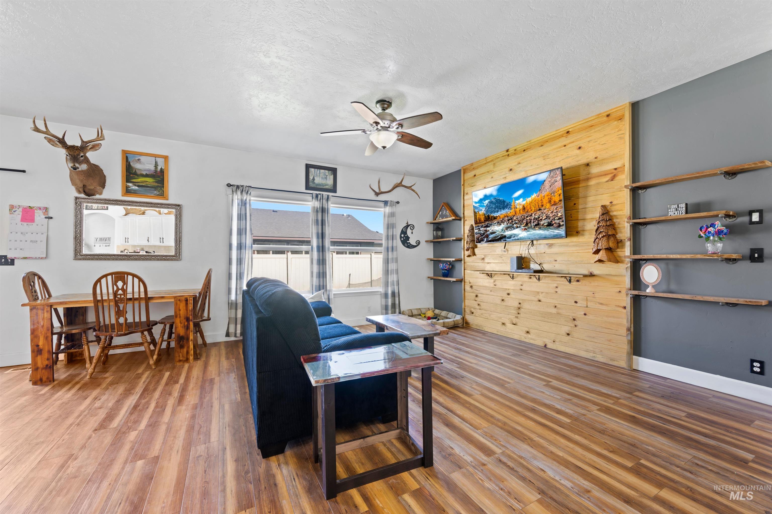 Living room with wooden walls, a textured ceiling, light wood-type flooring, and ceiling fan