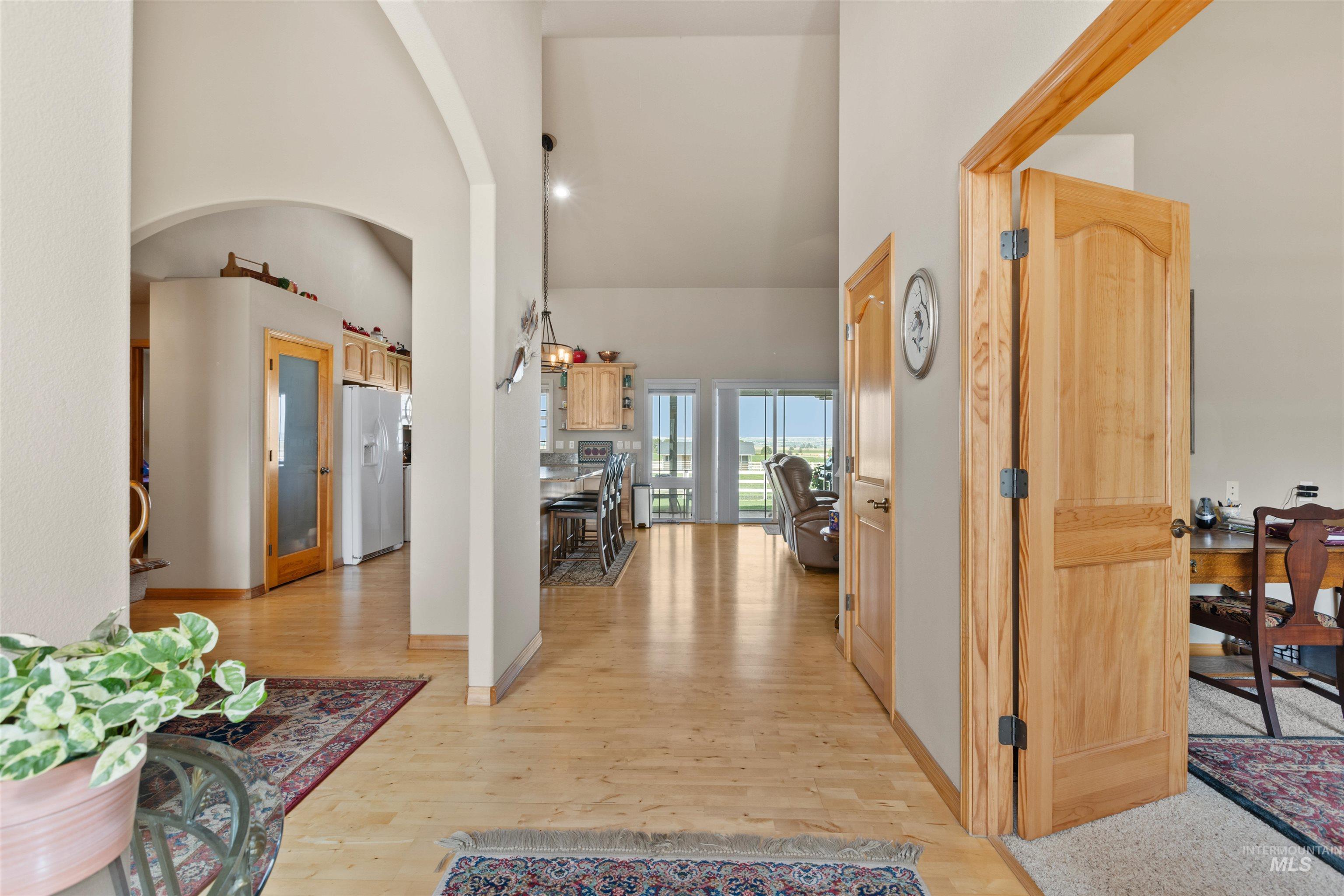 Hallway with a high ceiling, light wood finished floors, arched walkways, and an office area