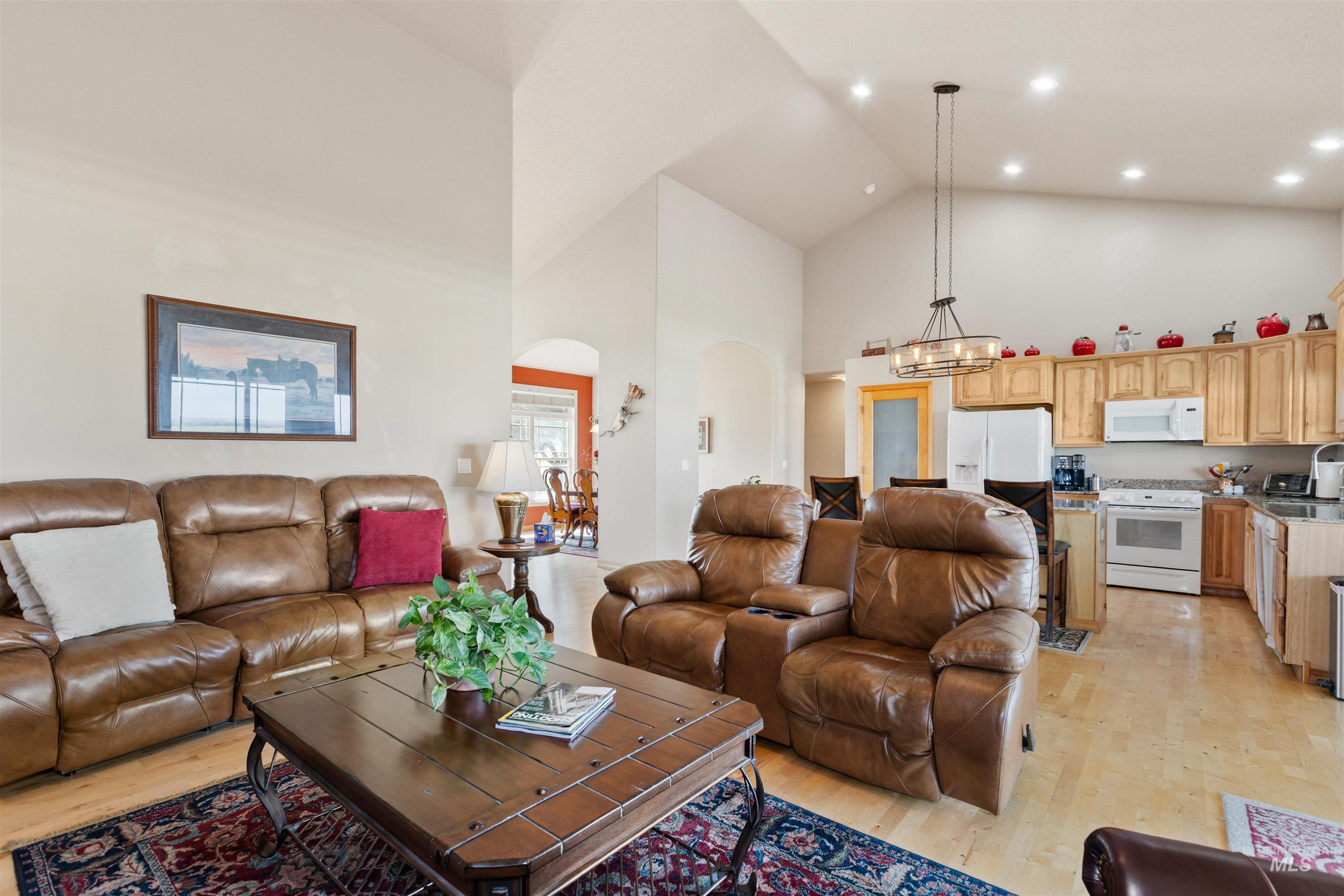 Living area featuring arched walkways, high vaulted ceiling, light wood-type flooring, a chandelier, and recessed lighting