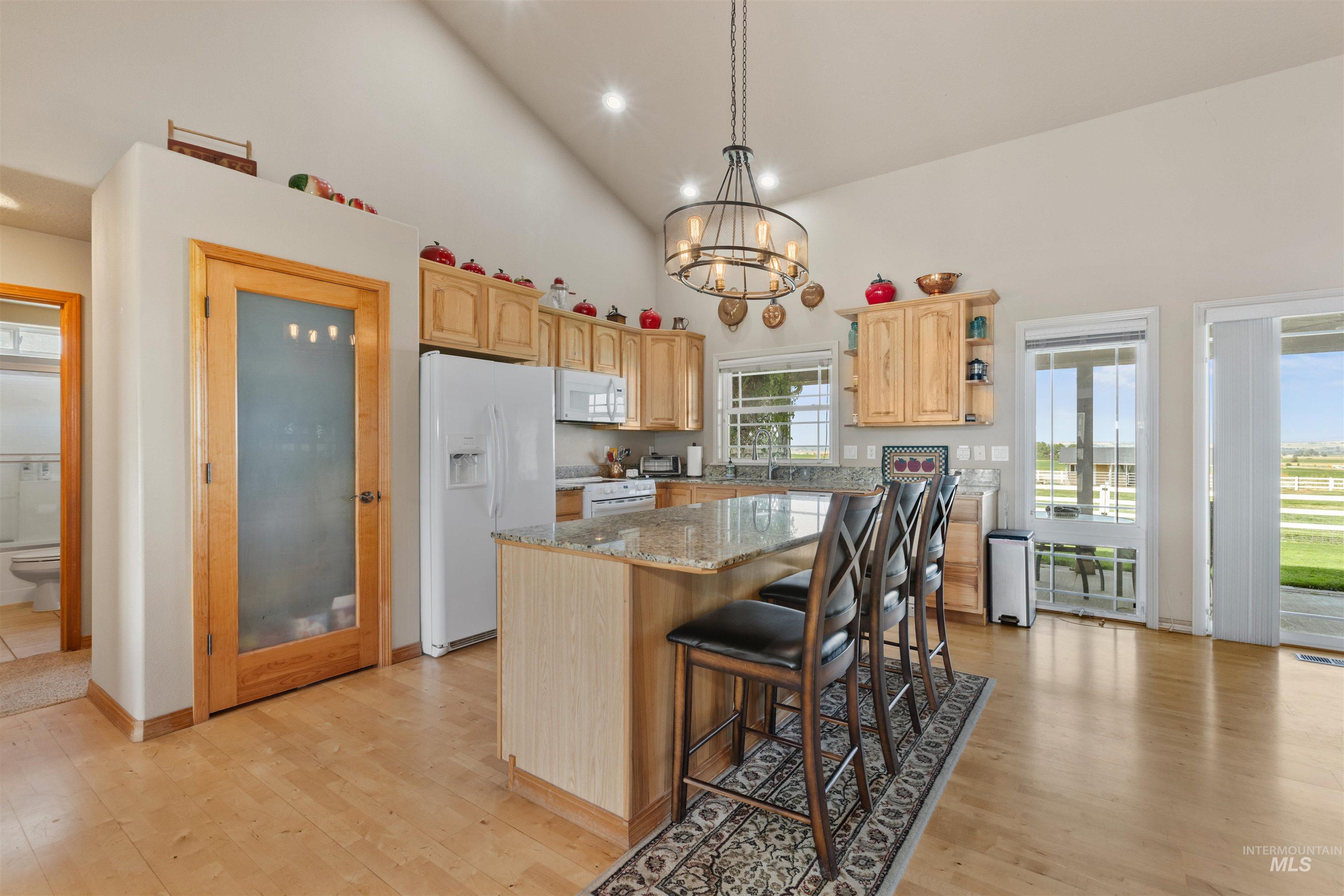 Kitchen with high vaulted ceiling, open shelves, light stone countertops, a center island, and white appliances