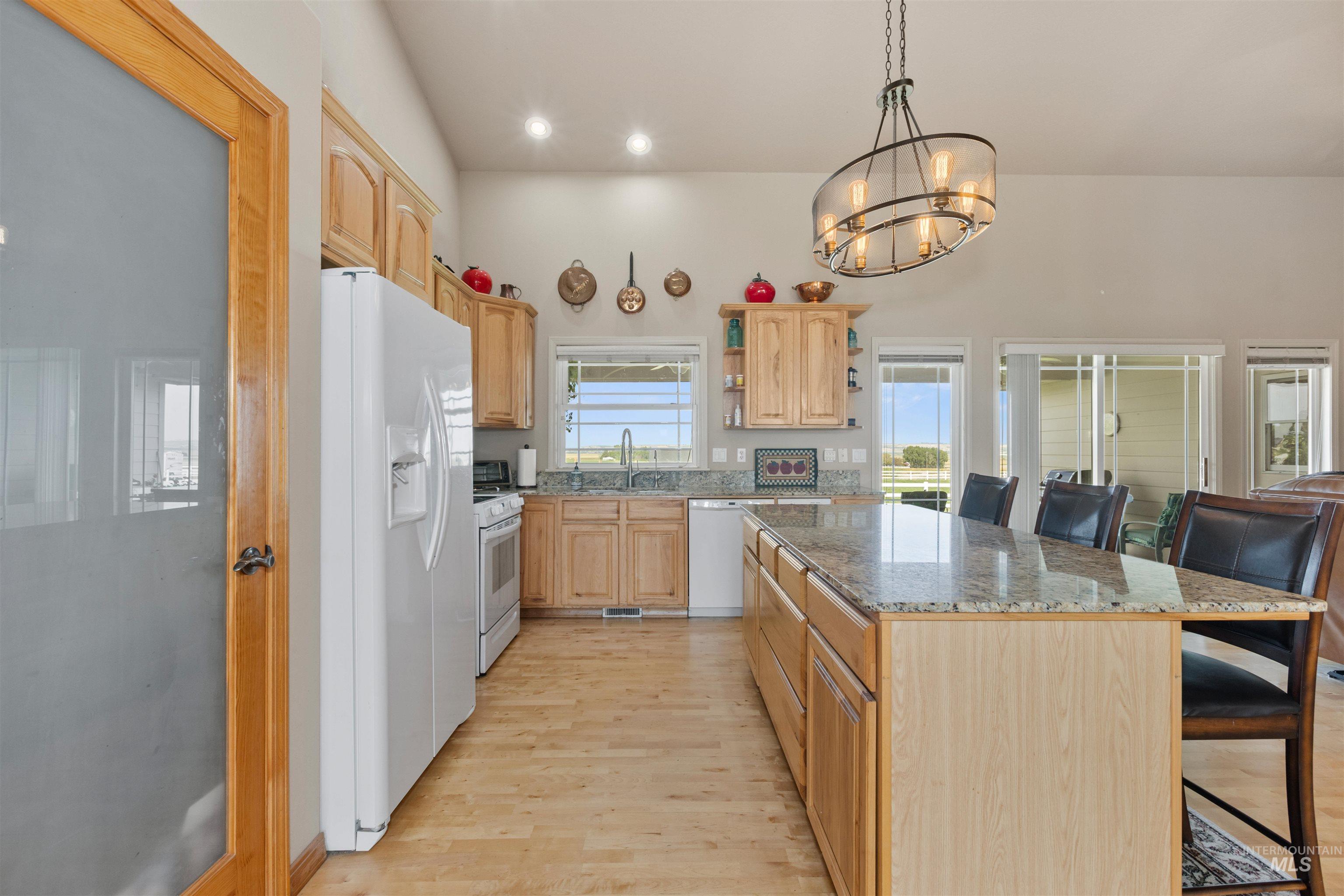 Kitchen featuring a breakfast bar, open shelves, white appliances, light brown cabinets, and light stone countertops