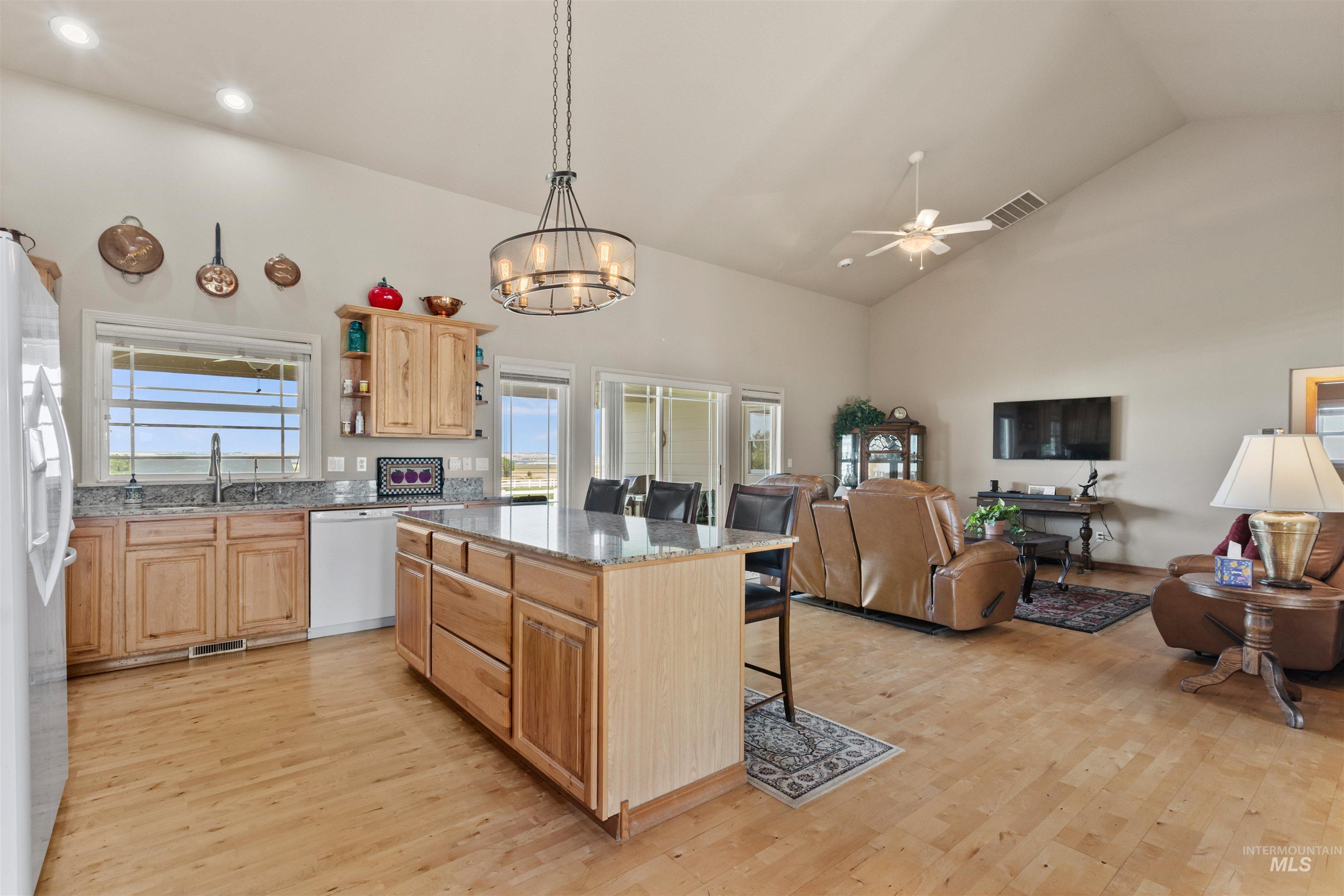 Kitchen with open shelves, light stone counters, open floor plan, light wood-style flooring, and high vaulted ceiling
