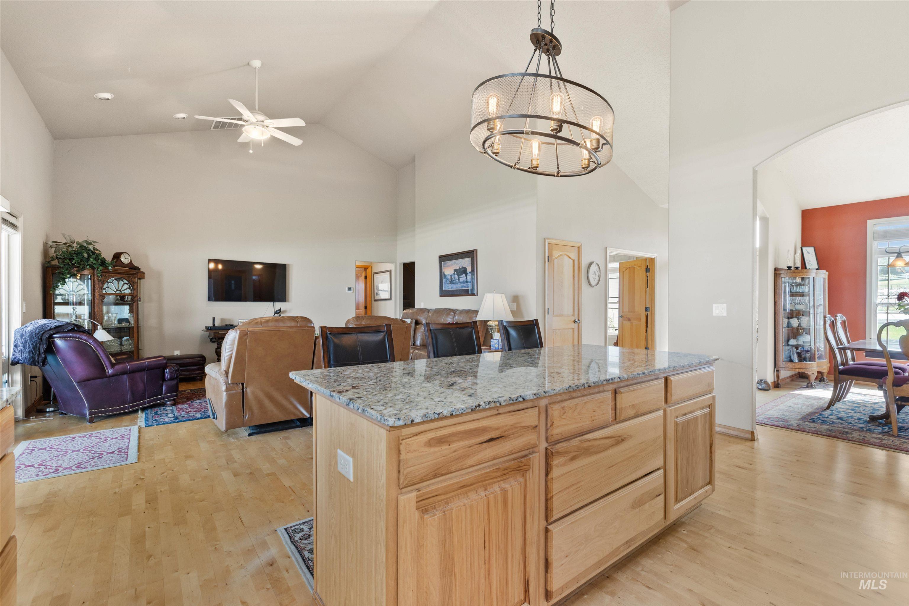 Kitchen featuring high vaulted ceiling, light brown cabinetry, a ceiling fan, light stone counters, and light wood-type flooring