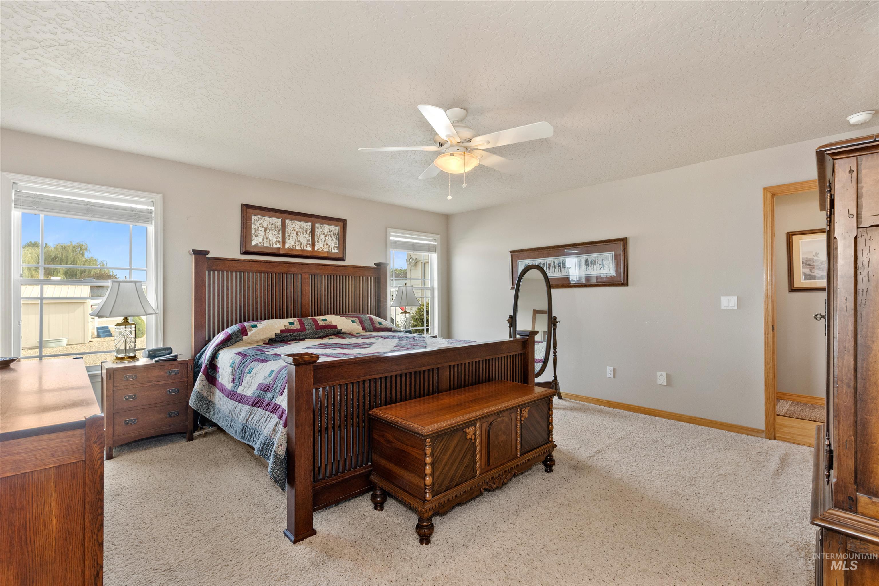 Bedroom with a textured ceiling, multiple windows, light carpet, and a ceiling fan