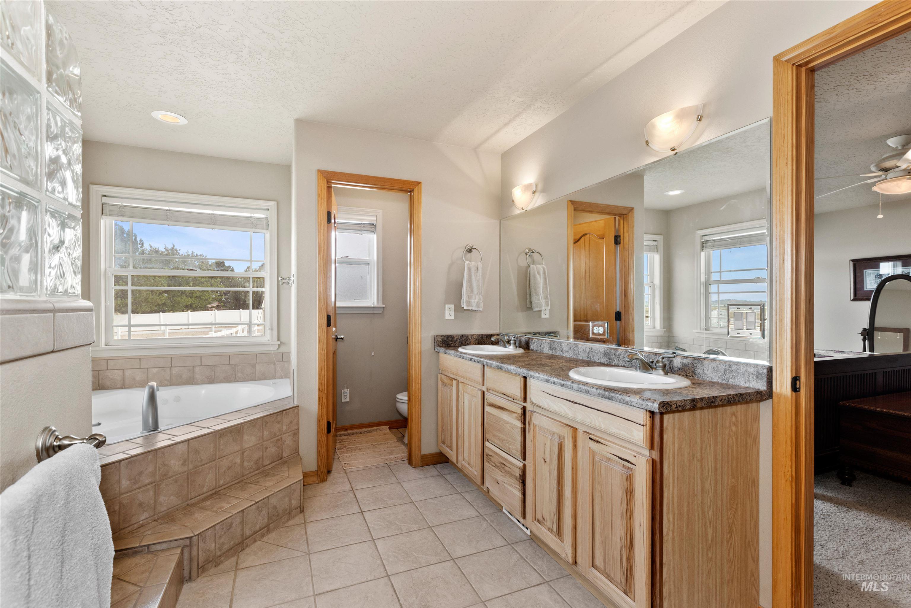 Full bathroom with double vanity, a bath, a textured ceiling, light tile patterned floors, and a ceiling fan