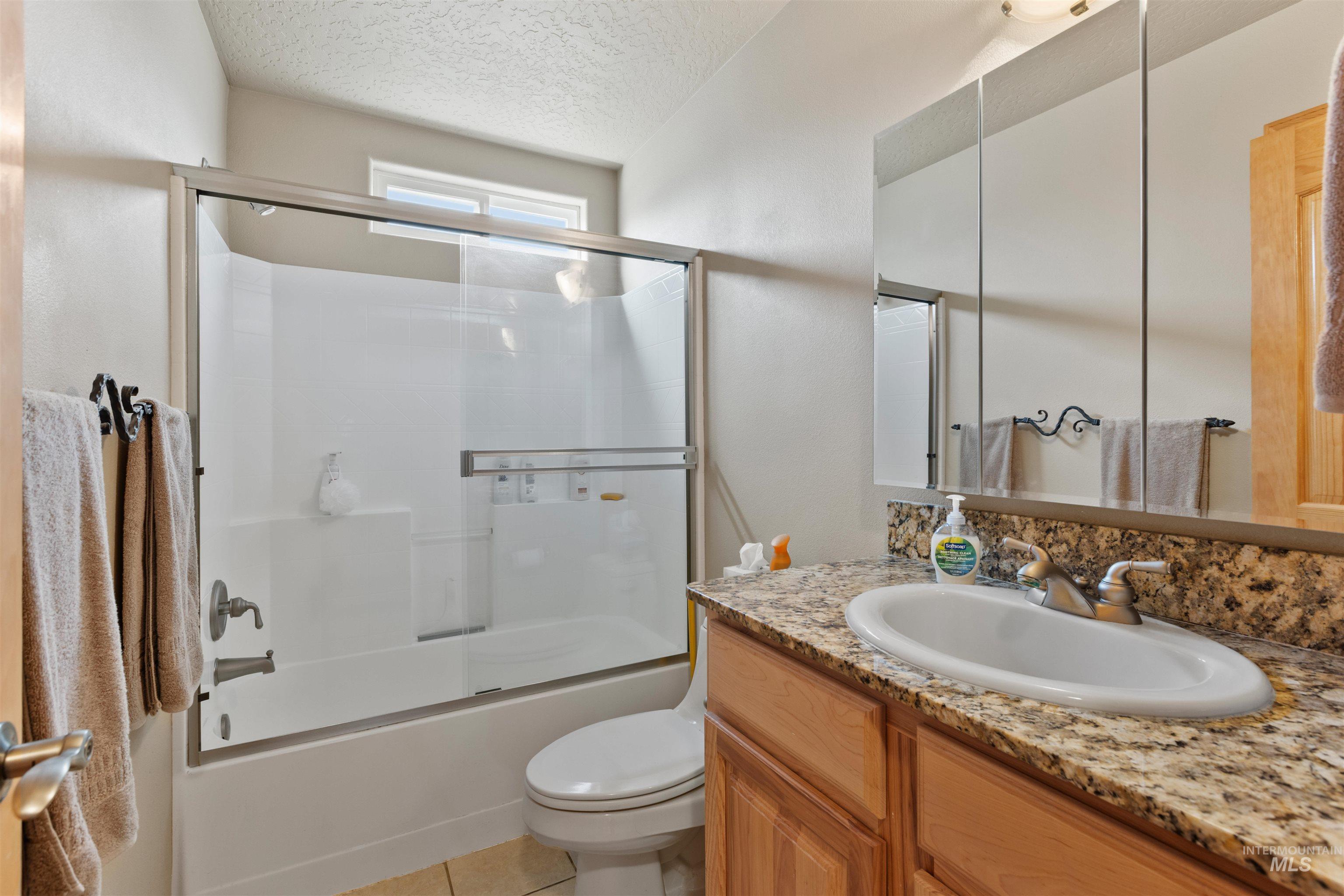 Full bathroom featuring enclosed tub / shower combo, a textured ceiling, vanity, and light tile patterned floors