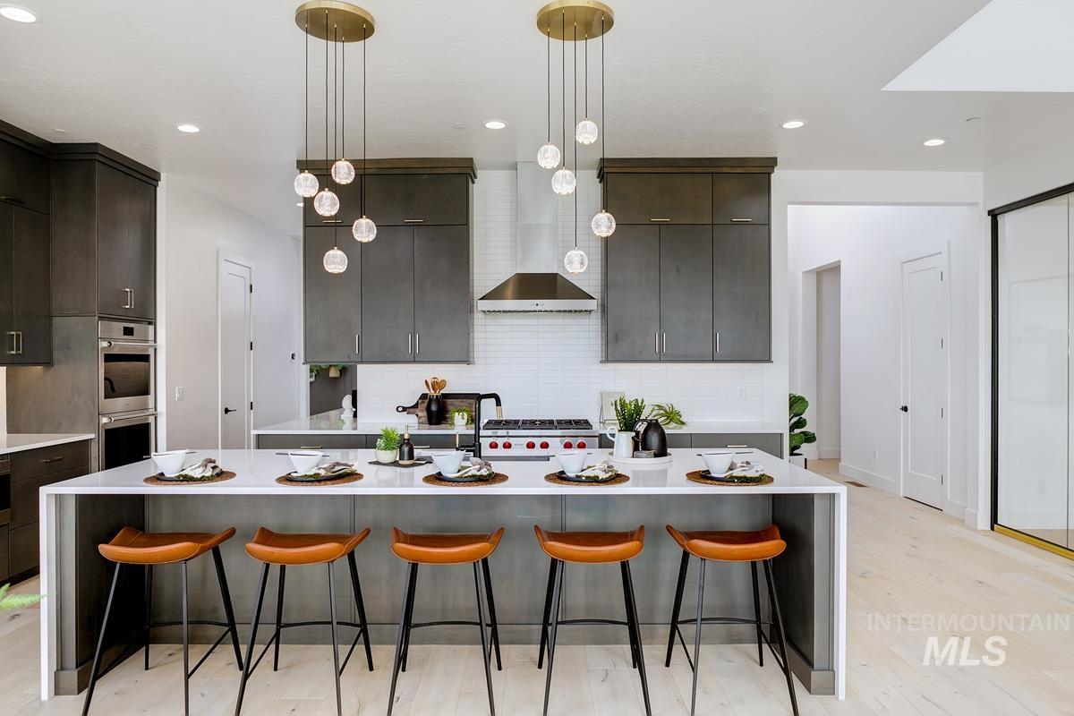 Kitchen with a kitchen breakfast bar, decorative light fixtures, decorative backsplash, a large island with sink, and wall chimney range hood
