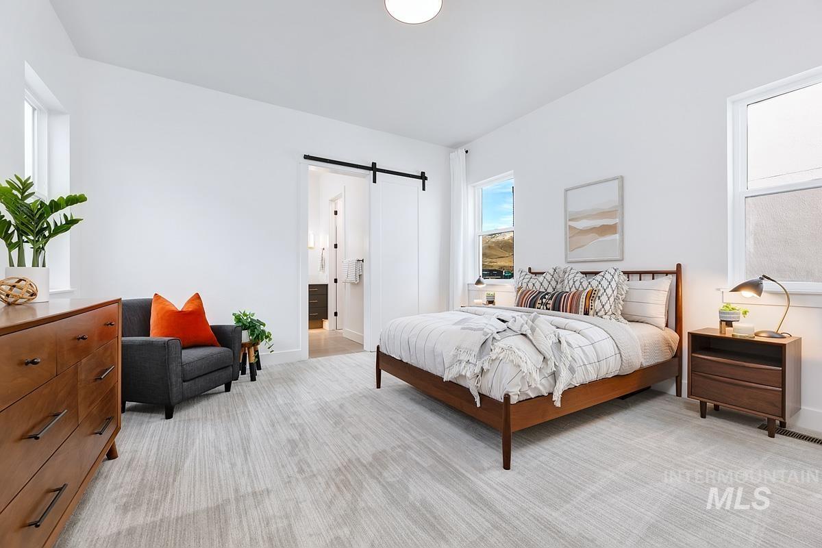 Bedroom with a barn door, light colored carpet, and ensuite bath