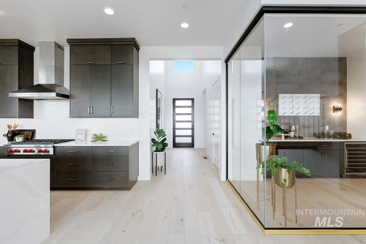 Kitchen featuring light wood-style flooring, wall chimney exhaust hood, modern cabinets, wine cooler, and backsplash