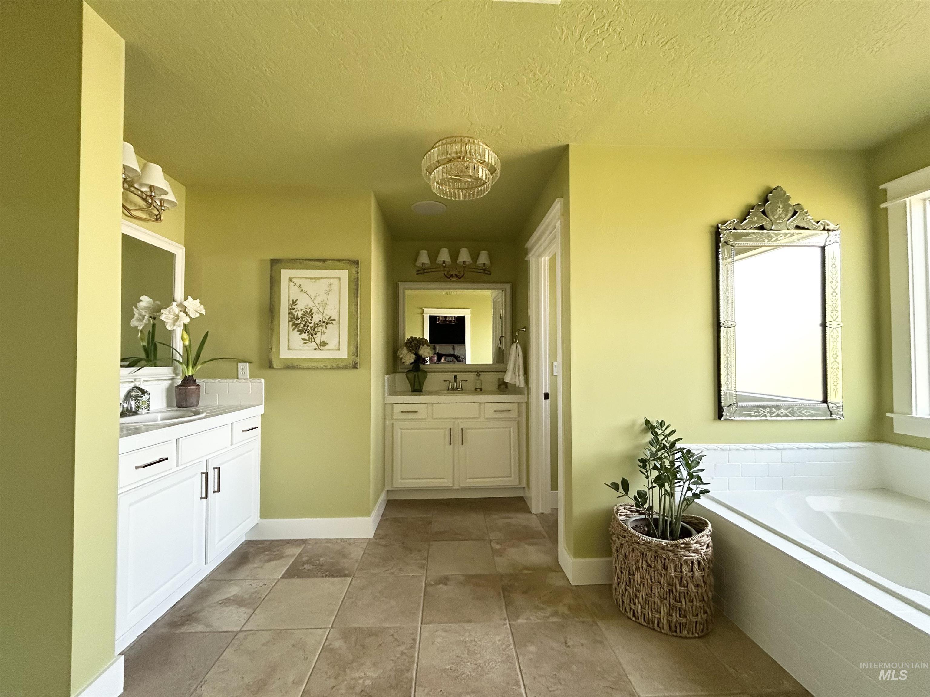 Bathroom featuring two vanities, a textured ceiling, and a bath