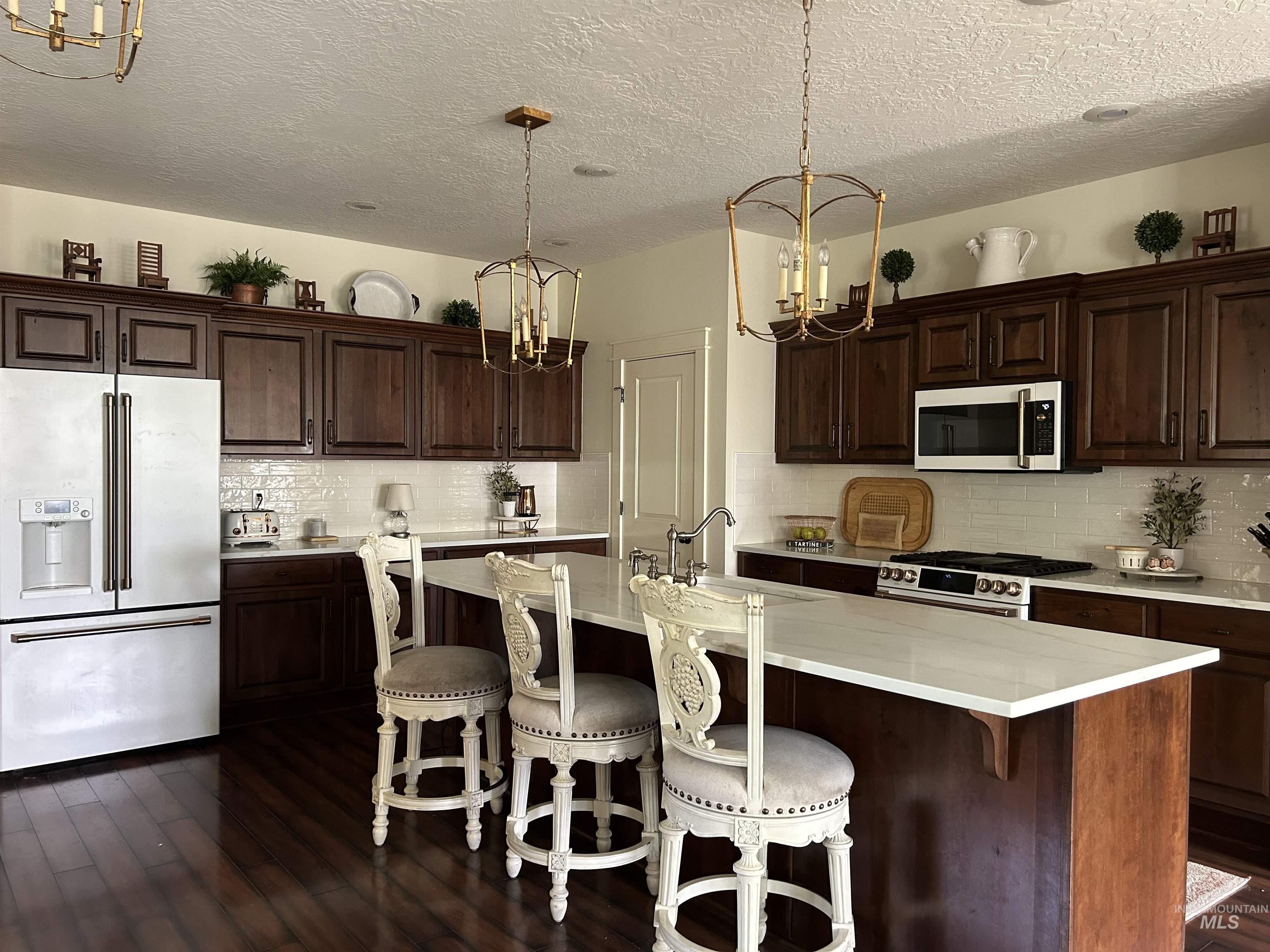 Kitchen with a kitchen breakfast bar, a chandelier, appliances with stainless steel finishes, dark brown cabinetry, and a textured ceiling