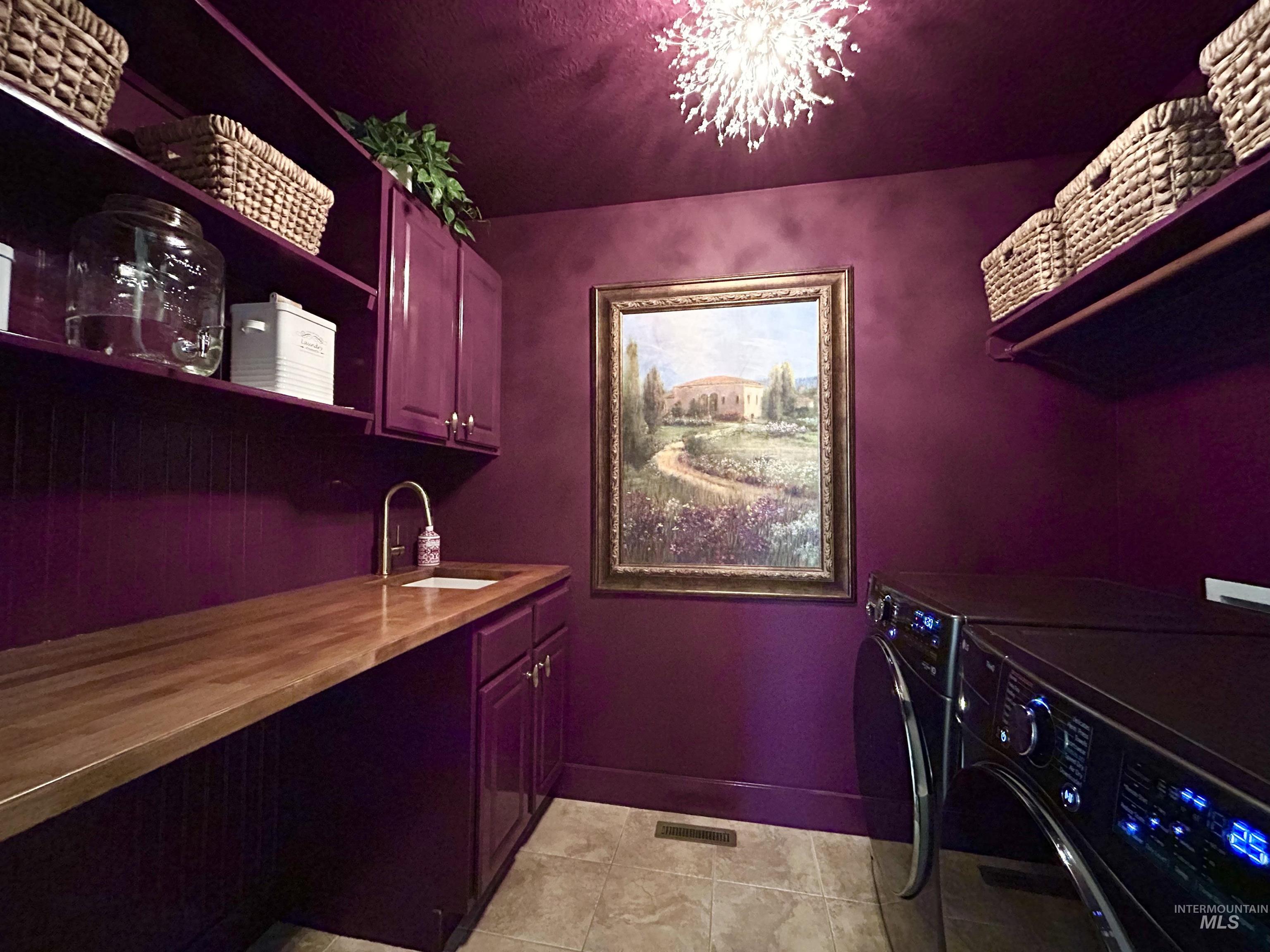 Laundry room with washer and dryer, cabinet space, a chandelier, and light tile patterned floors