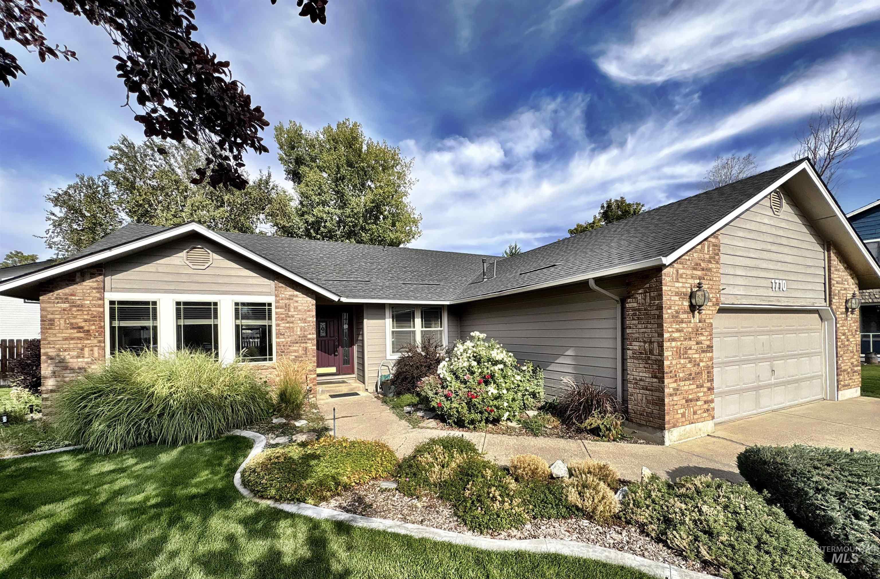 Ranch-style home featuring a garage, a shingled roof, brick siding, and a front lawn