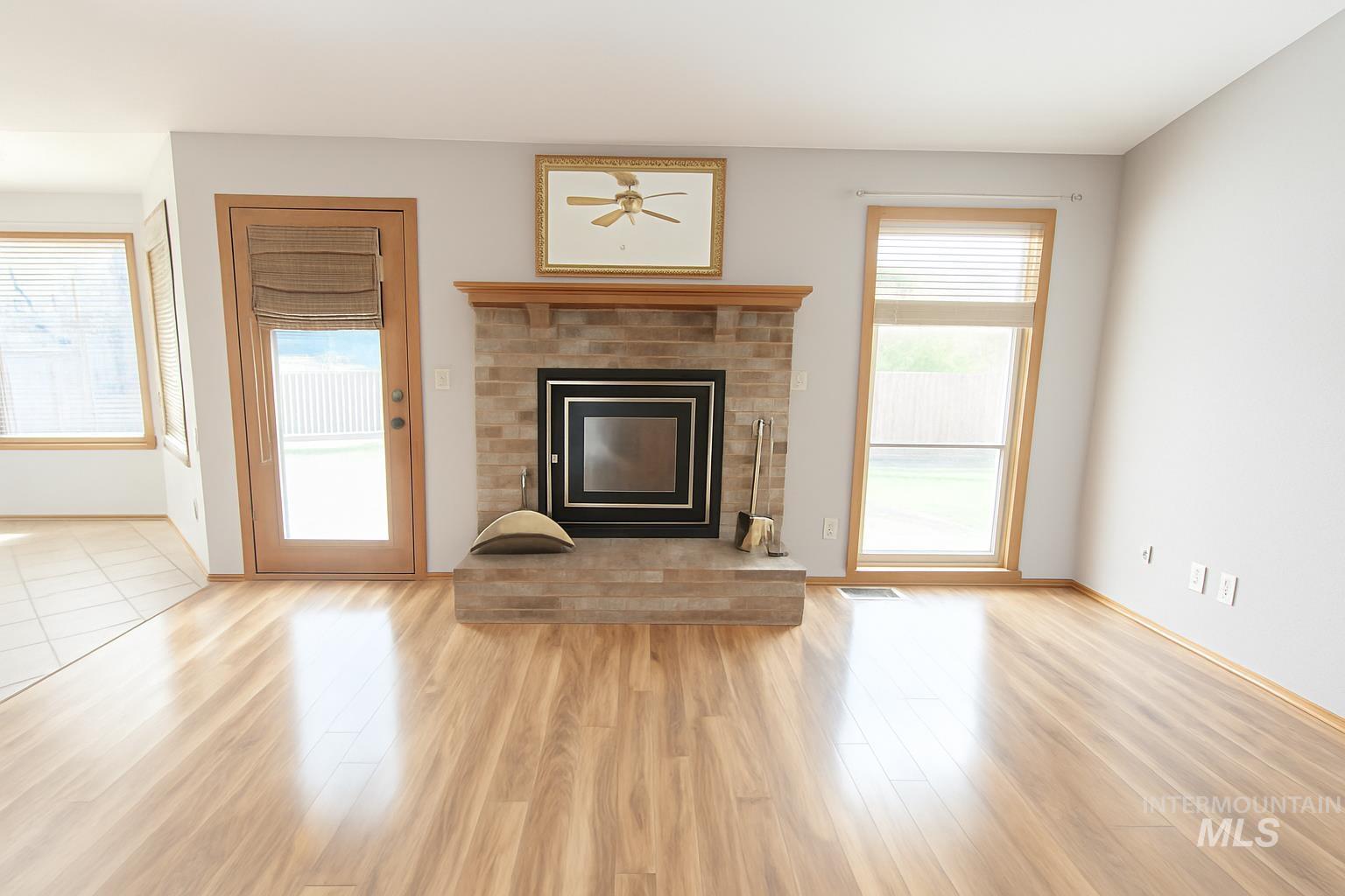 Unfurnished living room with a brick fireplace, light wood-type flooring, and a ceiling fan