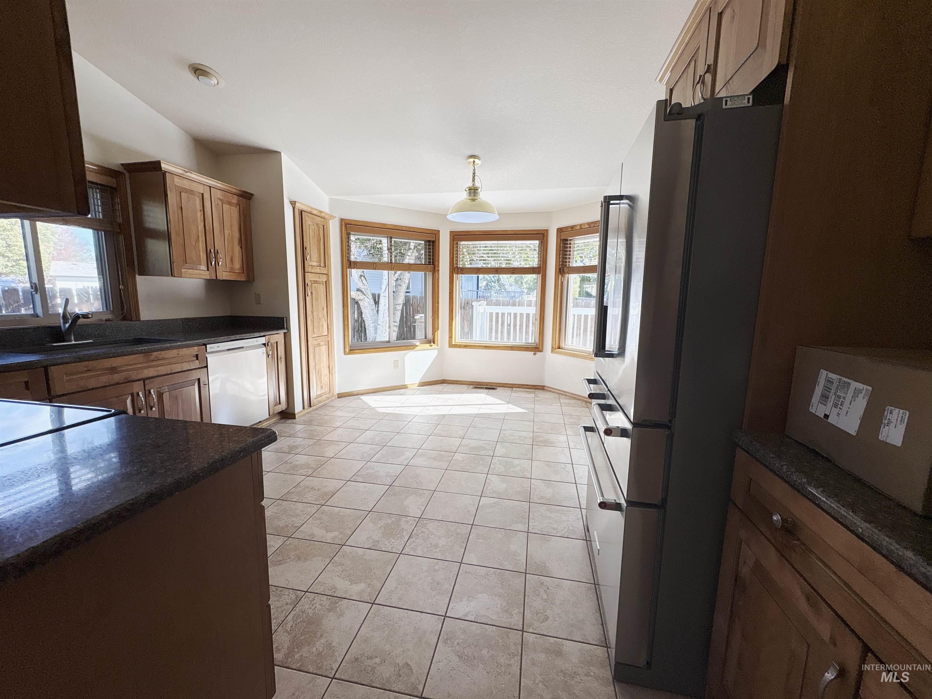 Kitchen featuring freestanding refrigerator, brown cabinetry, dark stone counters, dishwasher, and light tile patterned floors