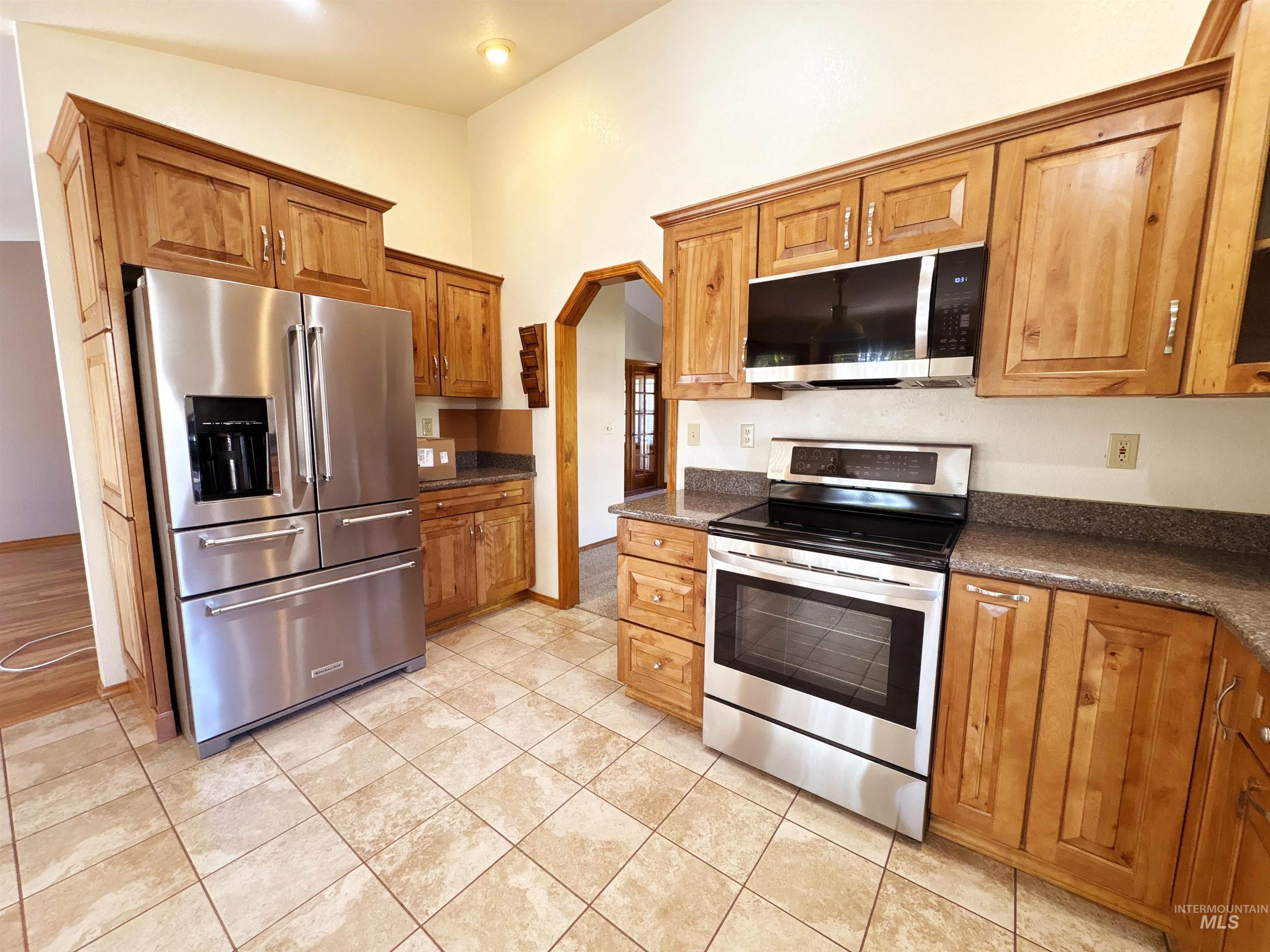 Kitchen with stainless steel appliances, brown cabinets, arched walkways, and light tile patterned flooring