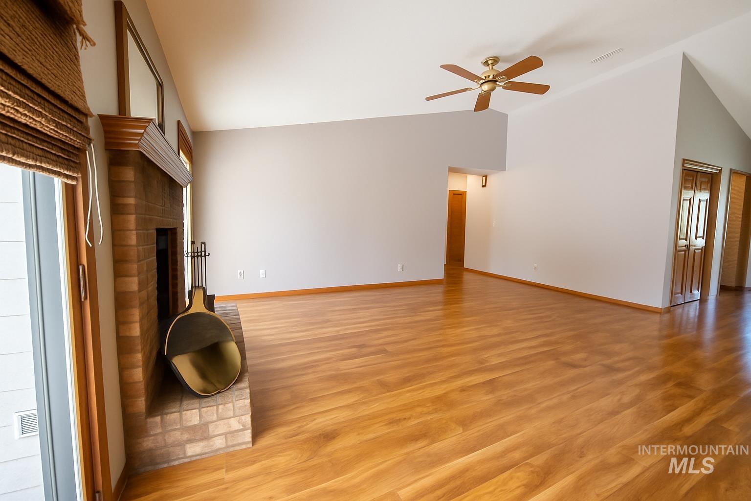 Unfurnished living room featuring light wood-type flooring, ceiling fan, a brick fireplace, and high vaulted ceiling