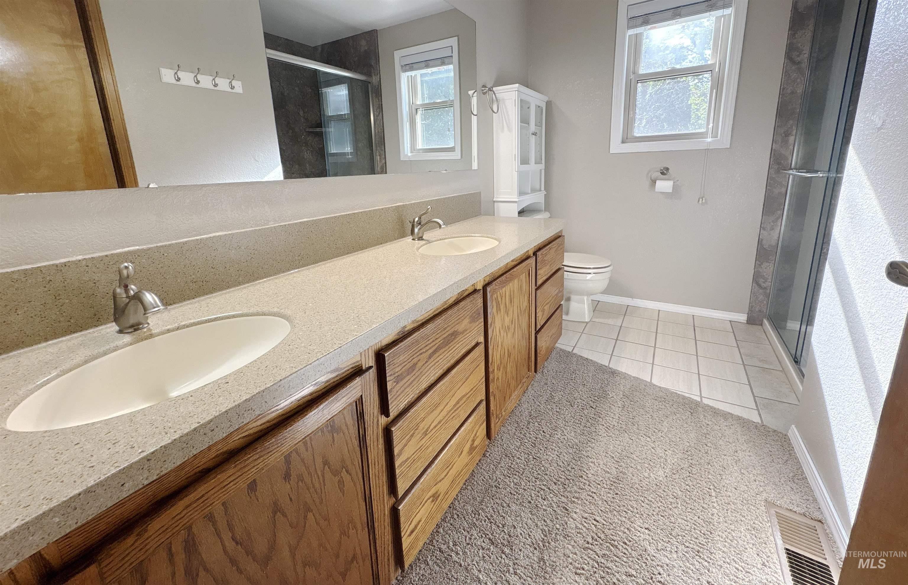 Bathroom featuring a shower stall, light tile patterned flooring, double vanity, and plenty of natural light