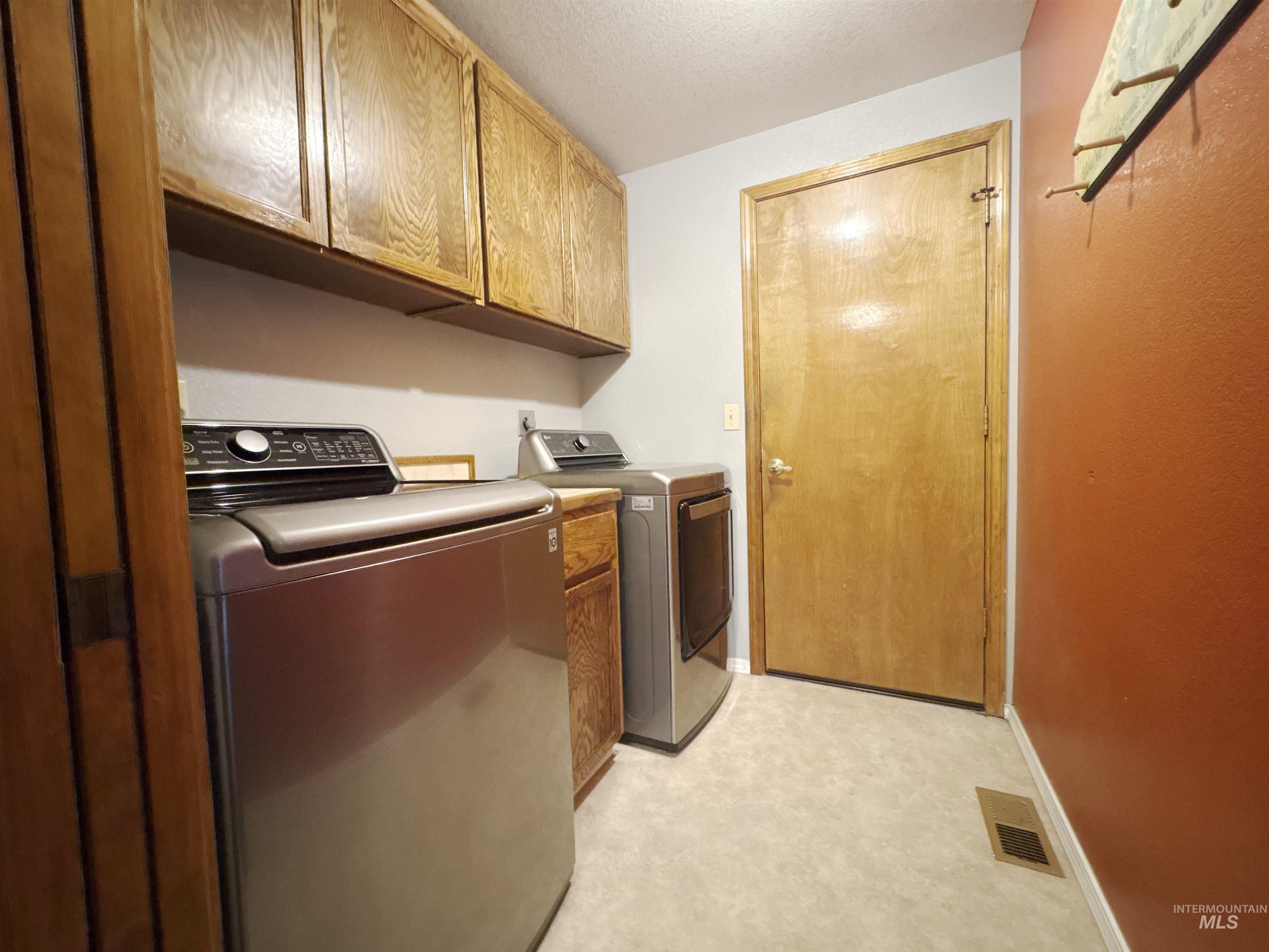 Laundry area featuring cabinet space, washing machine and clothes dryer, light flooring, and a textured ceiling