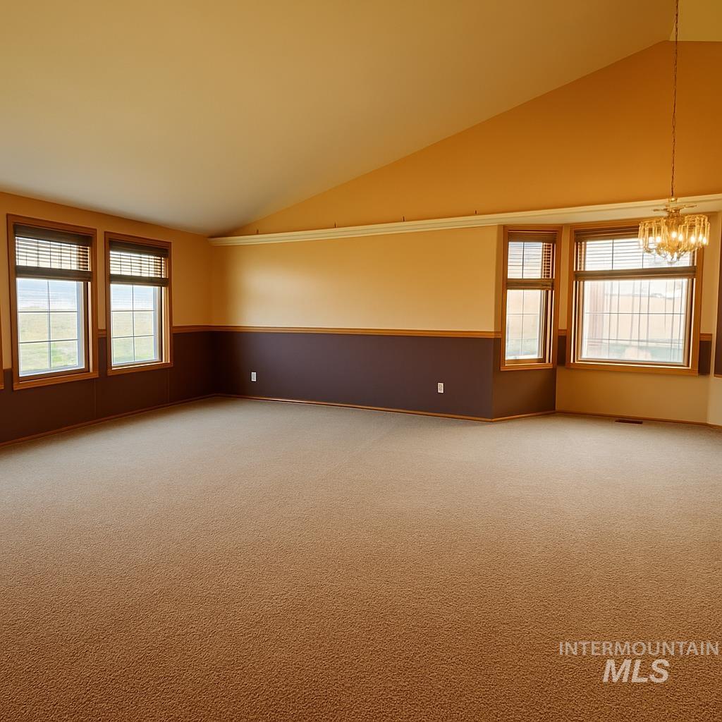 Empty room with vaulted ceiling, plenty of natural light, carpet floors, a wainscoted wall, and a chandelier