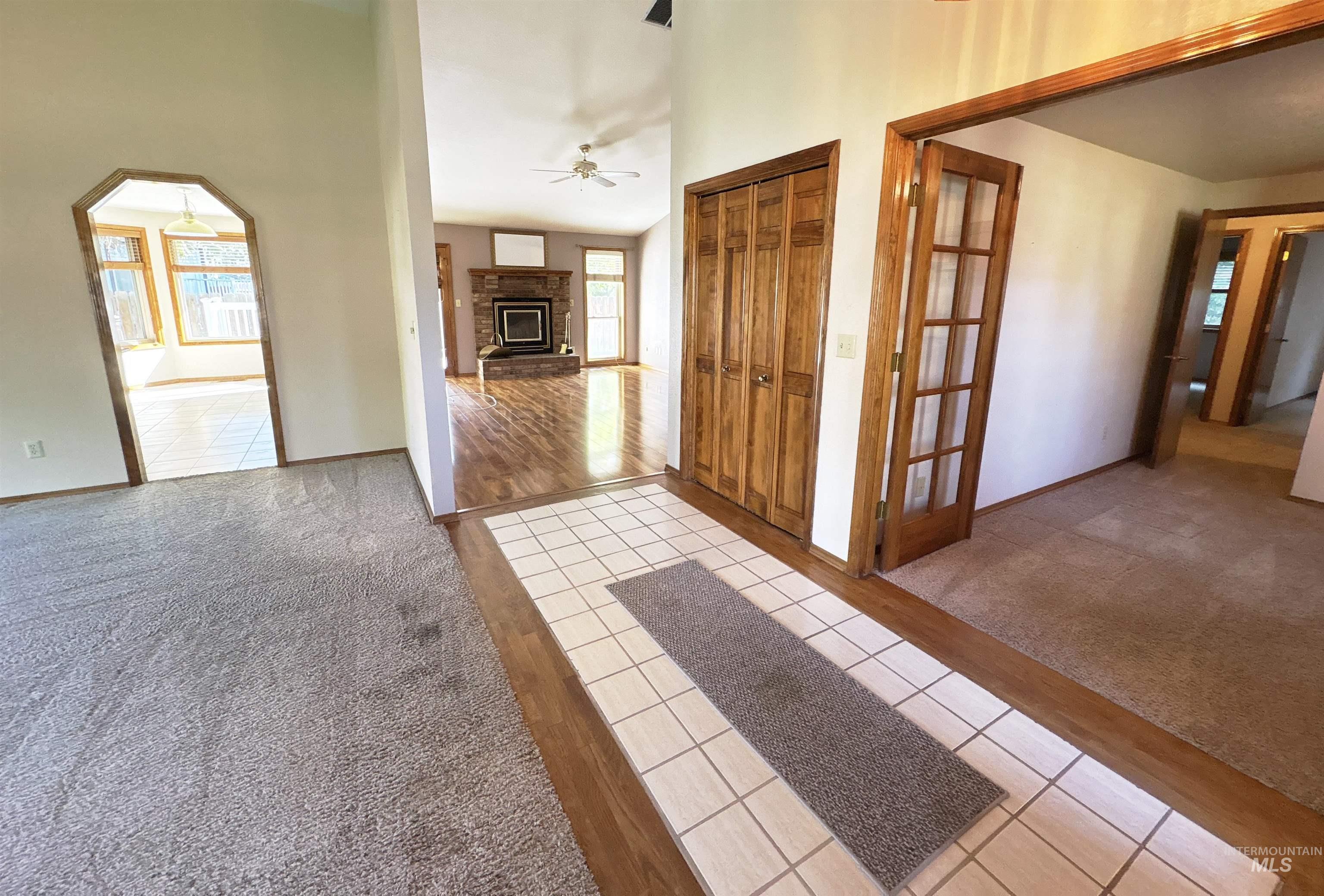 Entryway with light tile patterned floors, light colored carpet, a brick fireplace, and a ceiling fan