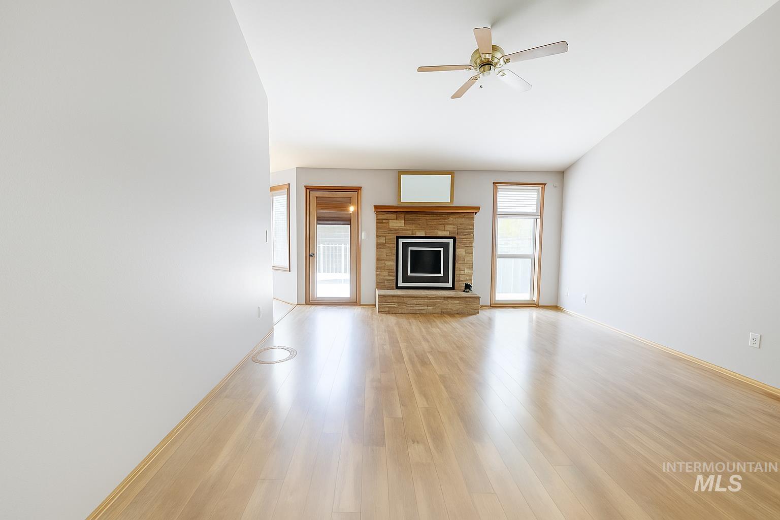 Unfurnished living room with wood finished floors, a stone fireplace, and ceiling fan