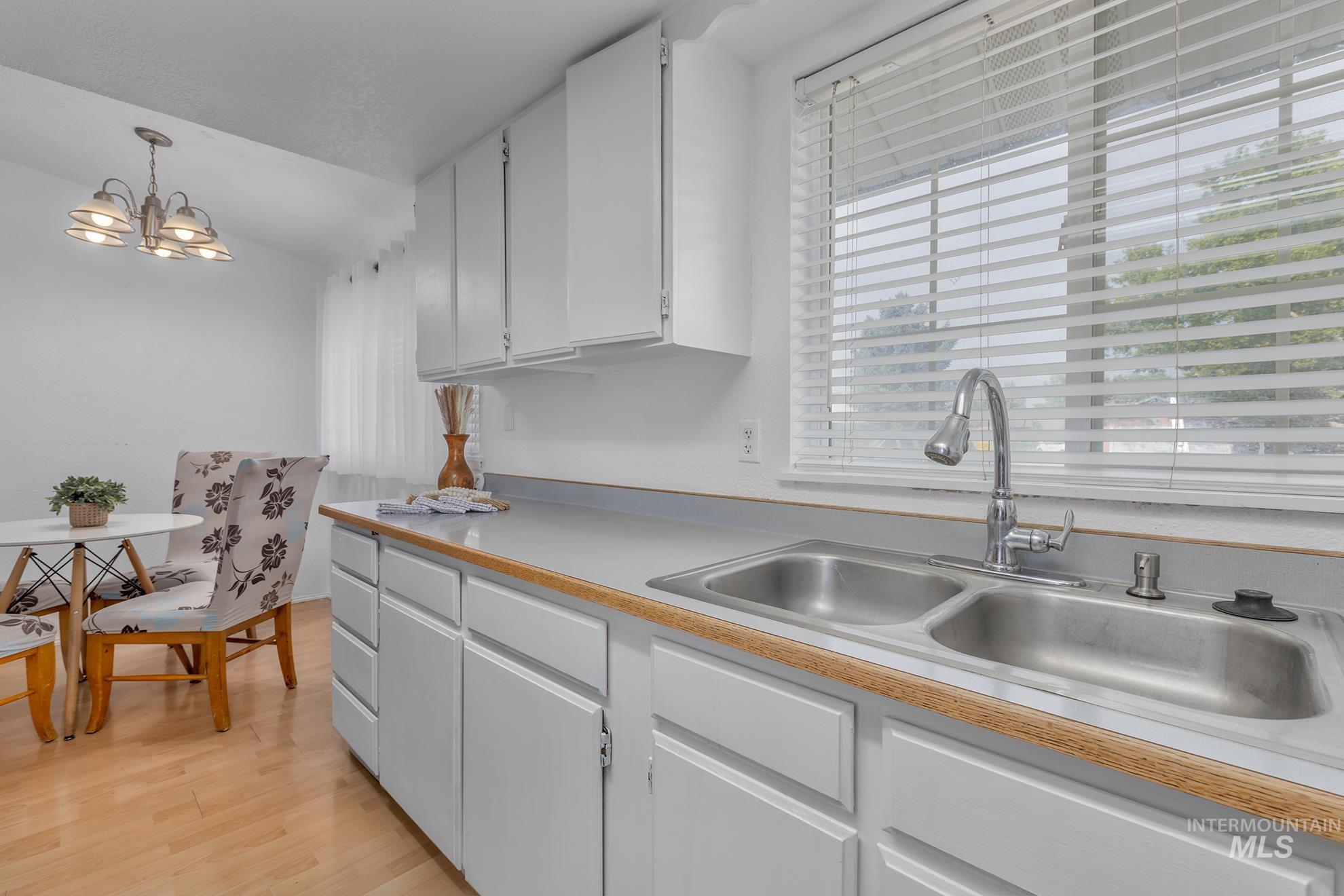Kitchen with white cabinets, pendant lighting, light countertops, light wood-style flooring, and a chandelier