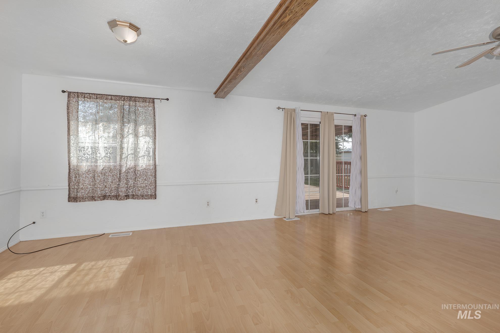 Empty room with wood finished floors, a ceiling fan, and beamed ceiling