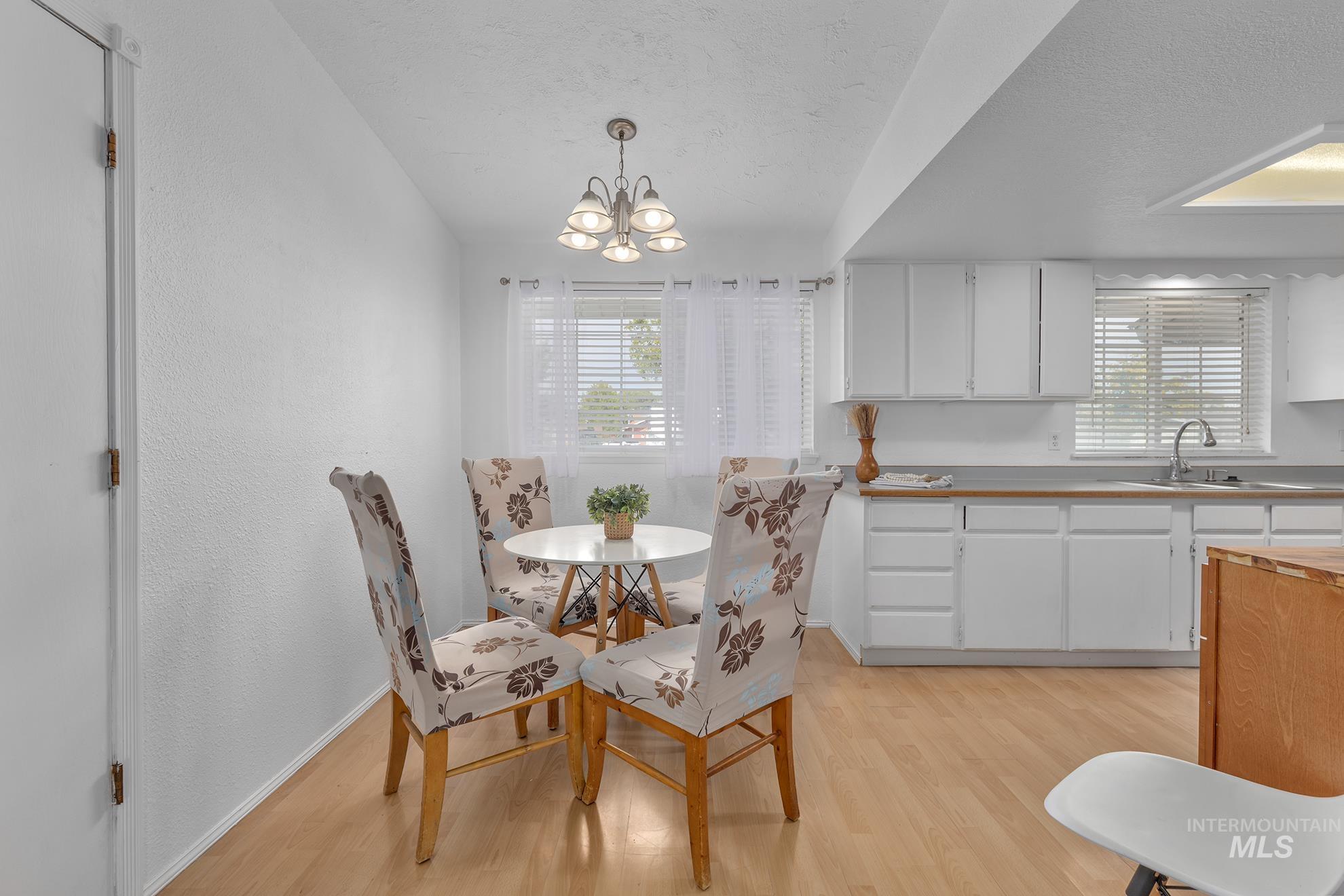 Dining space featuring light wood-style floors, a textured wall, a textured ceiling, and a chandelier