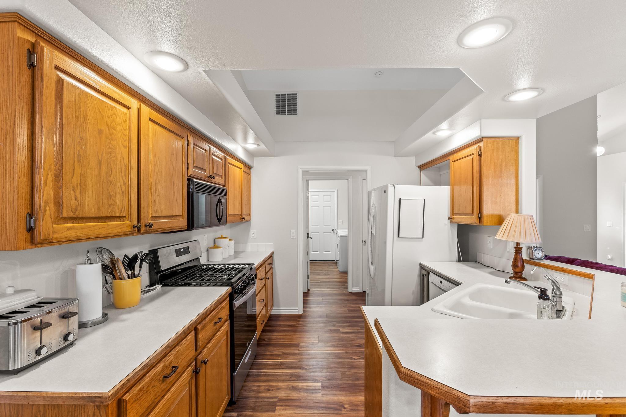 Kitchen featuring light countertops, stainless steel range with gas stovetop, dark wood-type flooring, and brown cabinetry