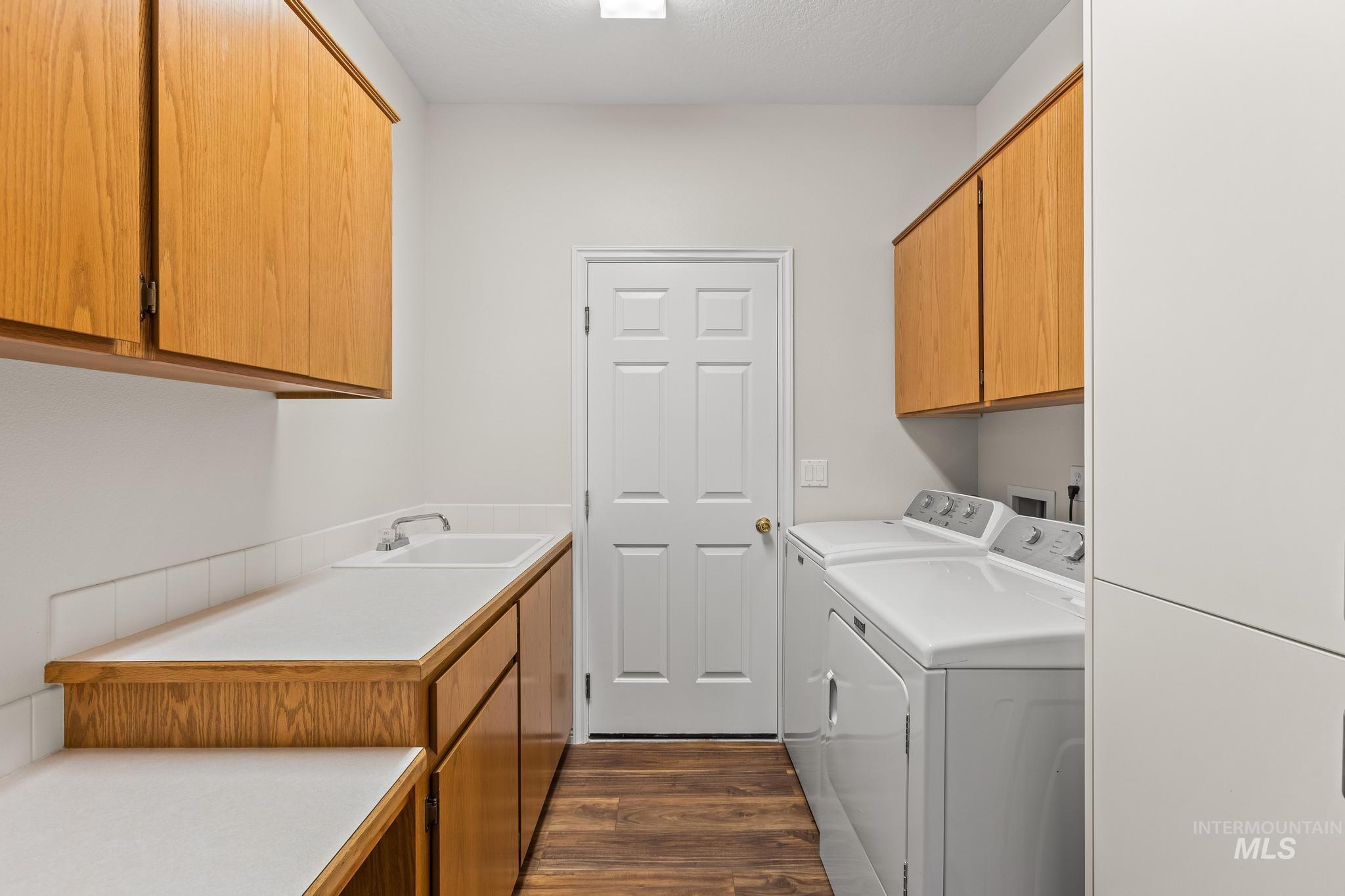 Laundry area with dark wood-style flooring, cabinet space, and washing machine and dryer