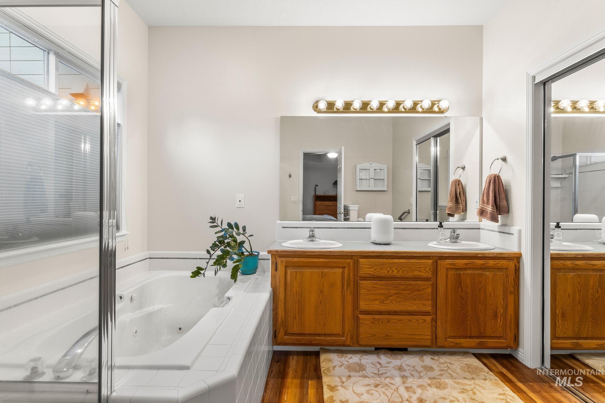 Bathroom with double vanity, a whirlpool tub, light wood-style flooring, and an enclosed shower