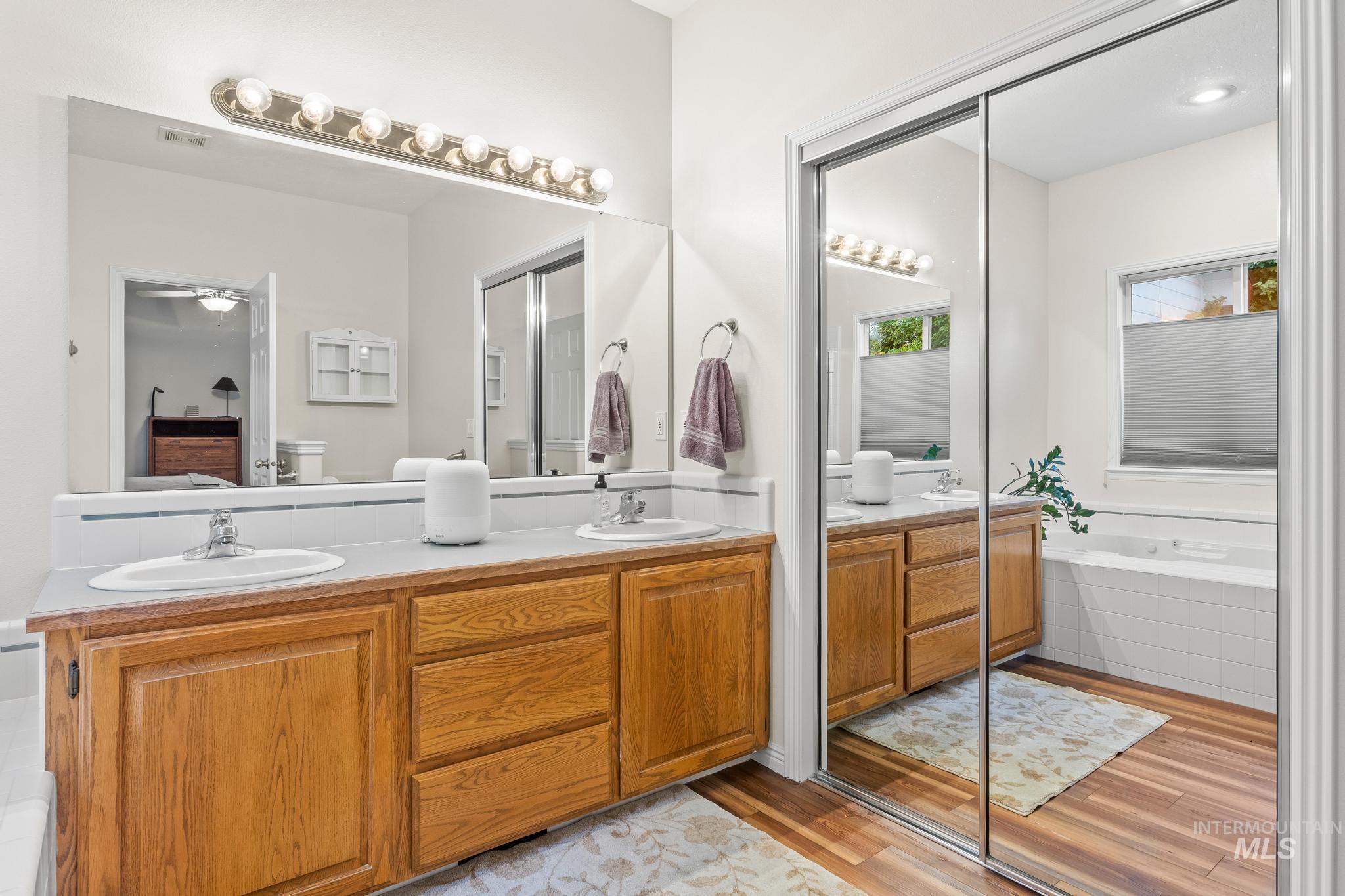 Full bath featuring double vanity, light wood-type flooring, and a bath
