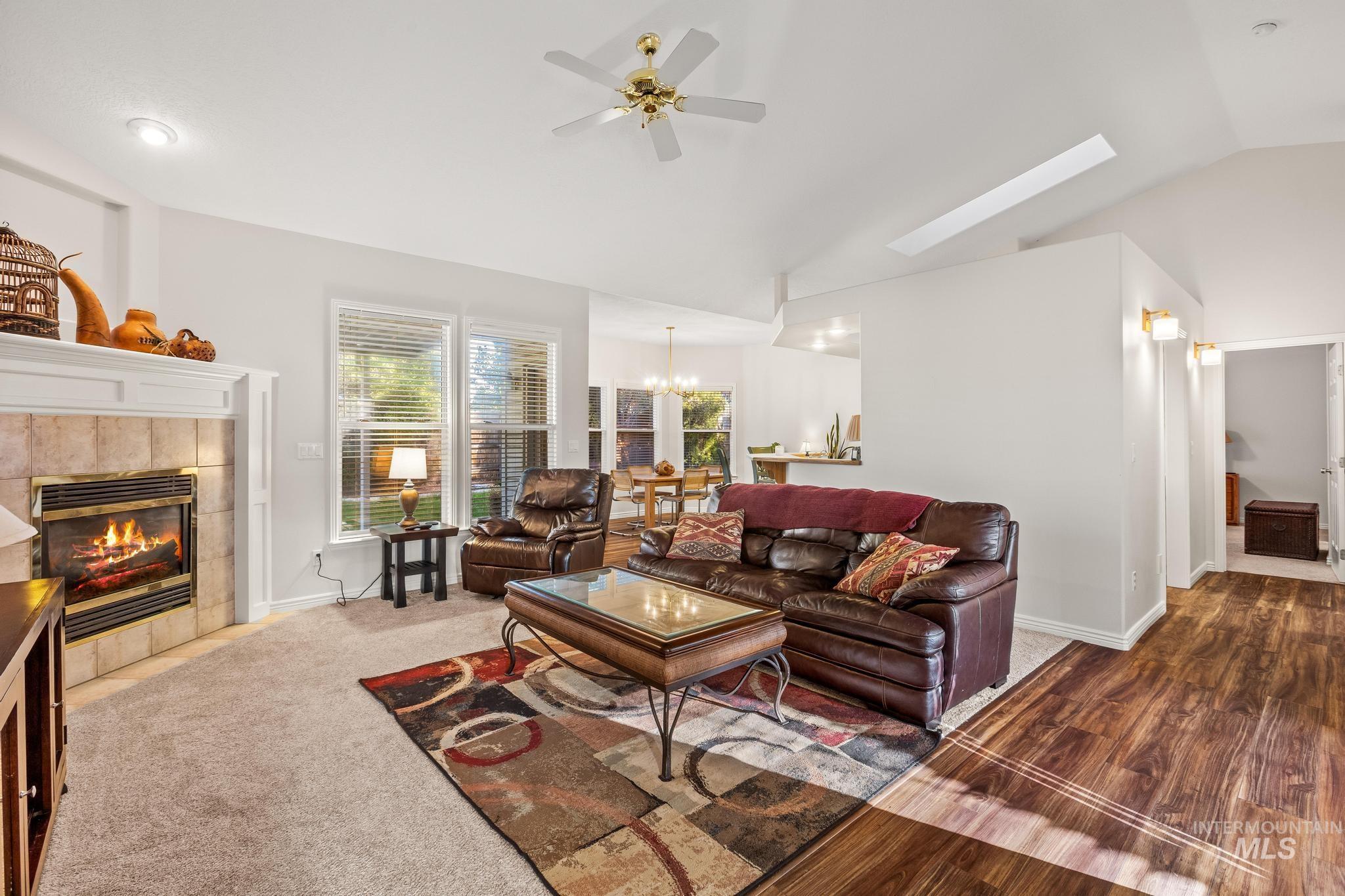 Living room featuring vaulted ceiling, a tiled fireplace, a chandelier, a ceiling fan, and a skylight