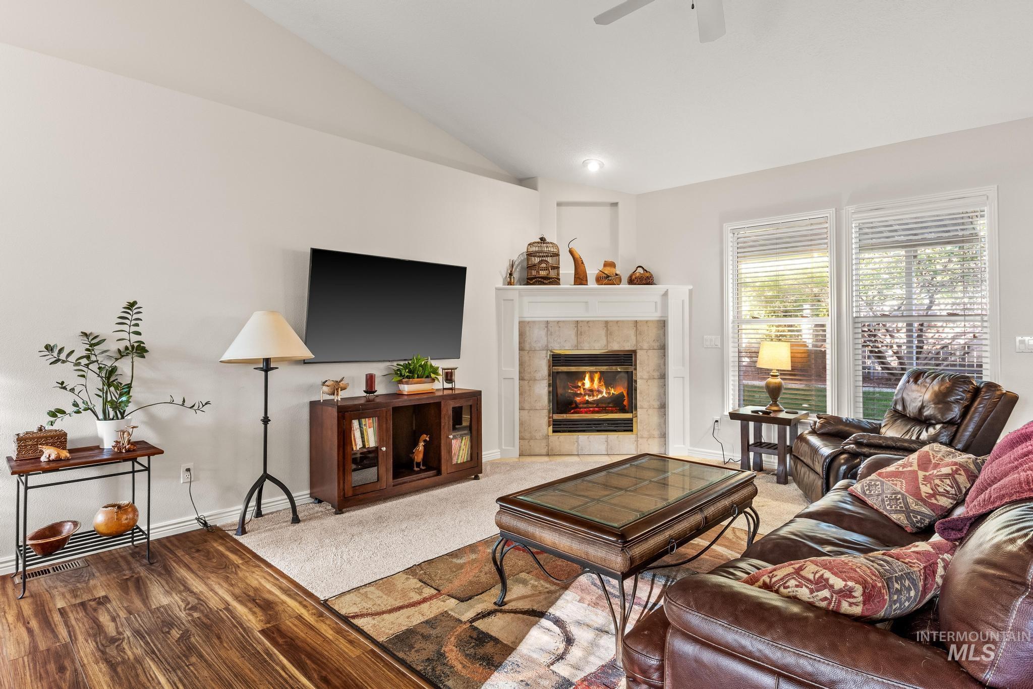 Living area with lofted ceiling, a tile fireplace, wood finished floors, and carpet flooring
