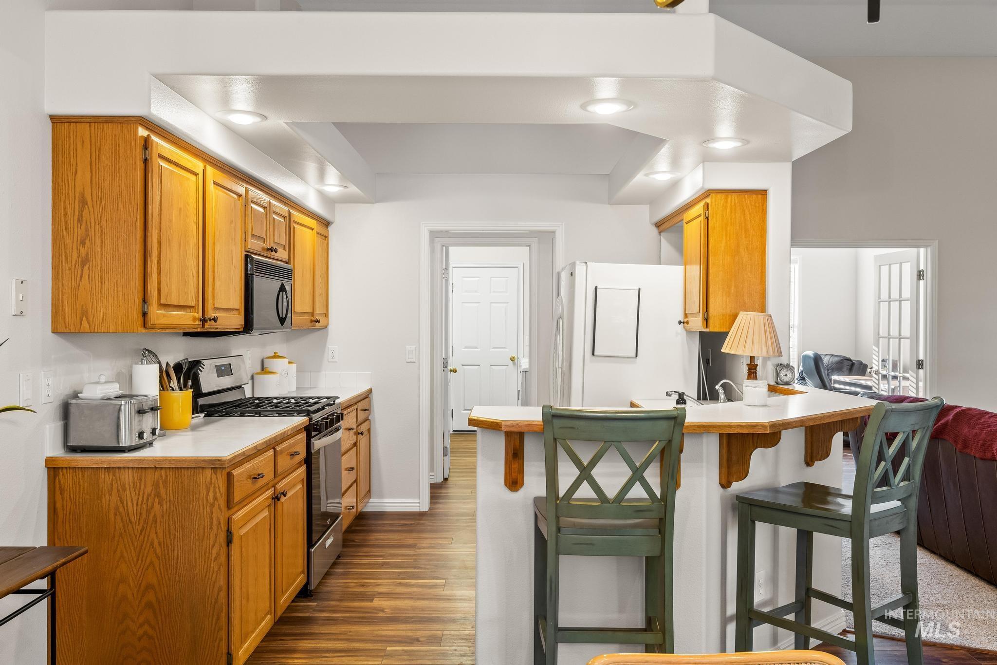Kitchen with light countertops, stainless steel gas range oven, a breakfast bar area, and dark wood-type flooring