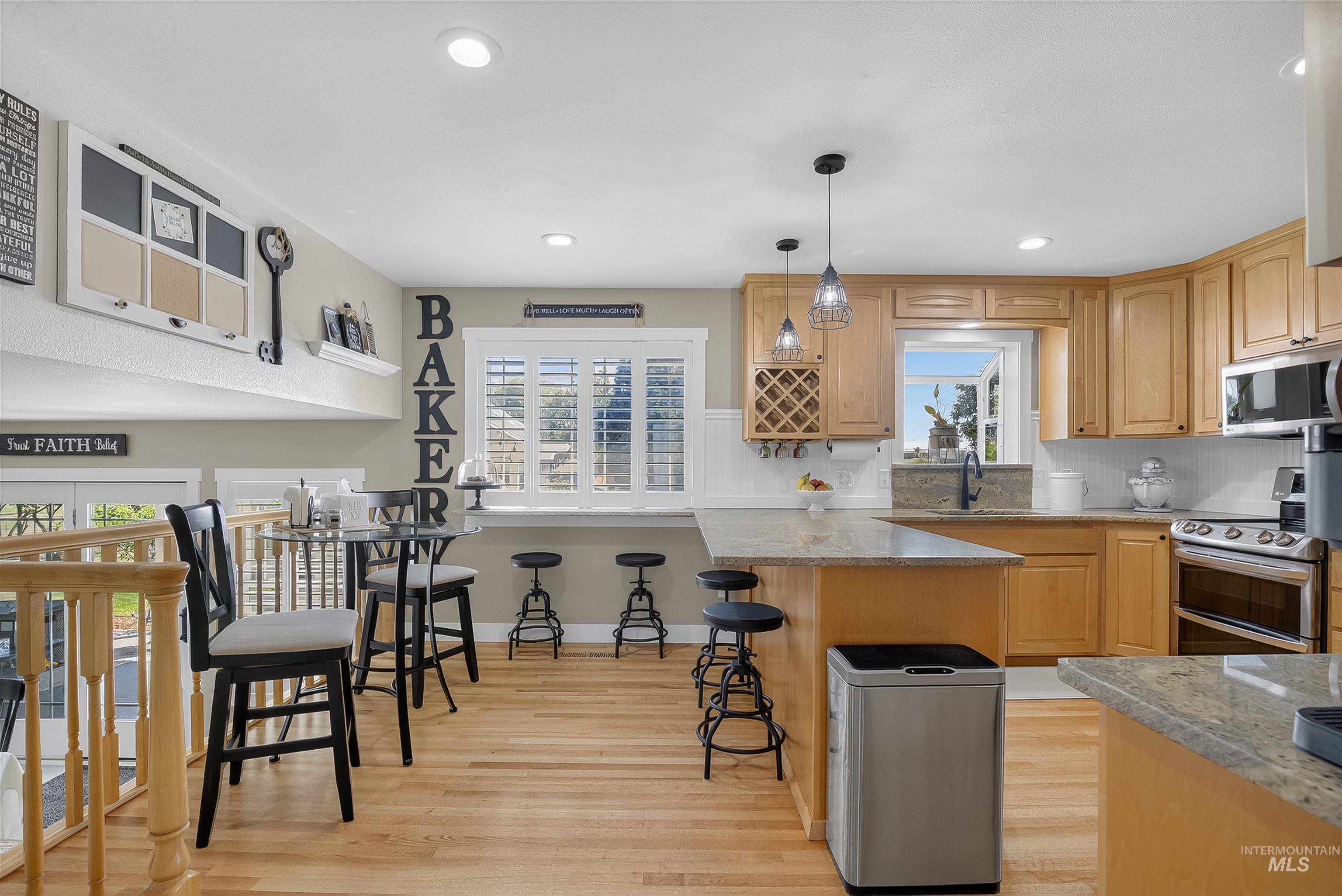 Kitchen with backsplash, stainless steel appliances, light wood finished floors, light stone counters, and pendant lighting