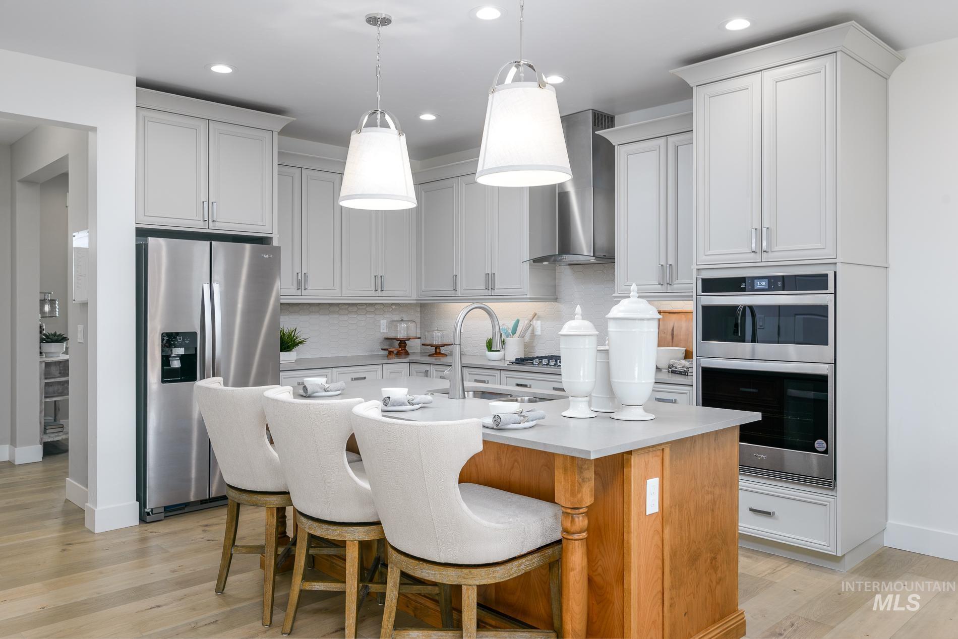 Kitchen with appliances with stainless steel finishes, a kitchen island with sink, light wood-type flooring, a kitchen breakfast bar, and decorative light fixtures