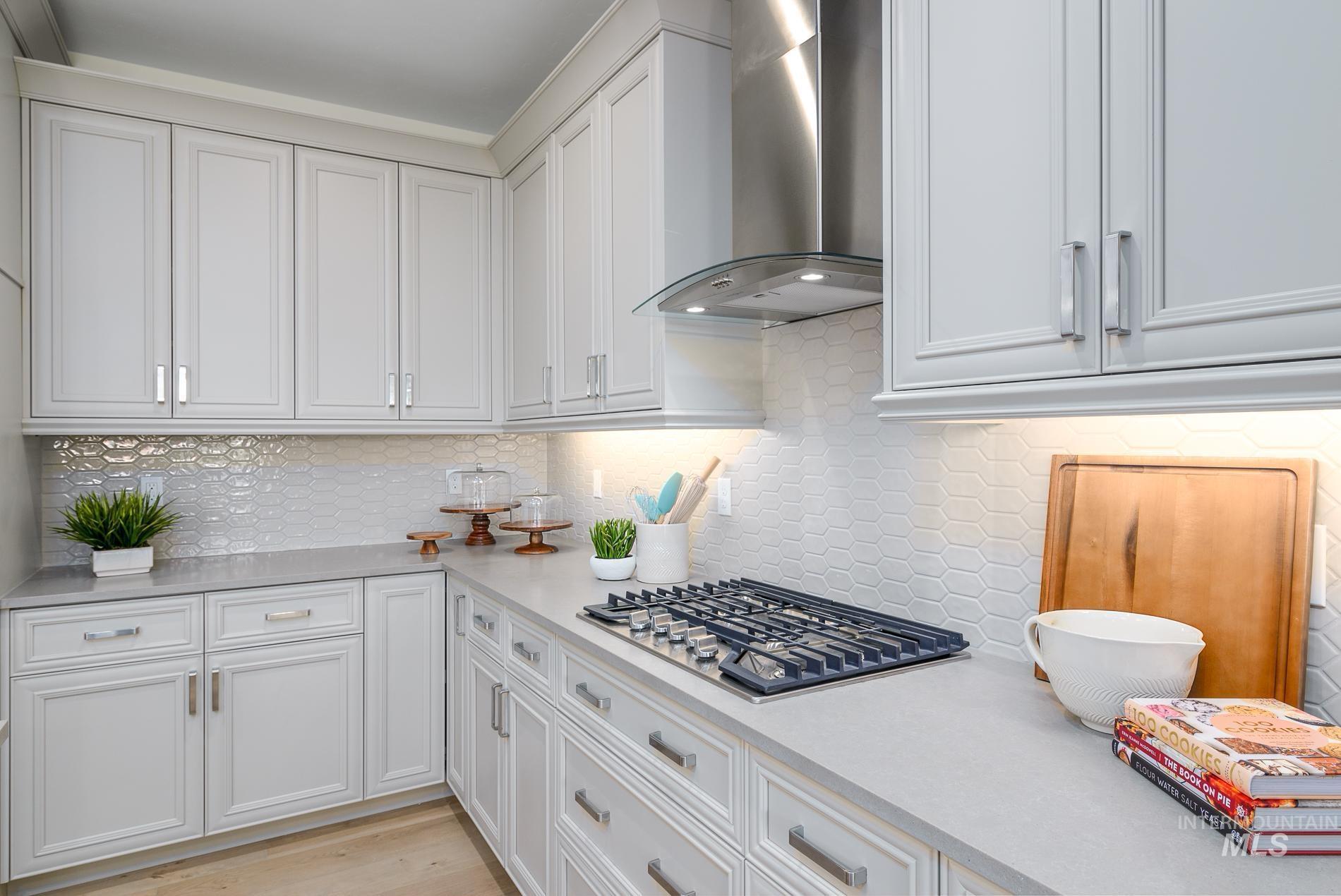 Kitchen featuring wall chimney range hood, white cabinets, stainless steel gas stovetop, decorative backsplash, and light wood-type flooring