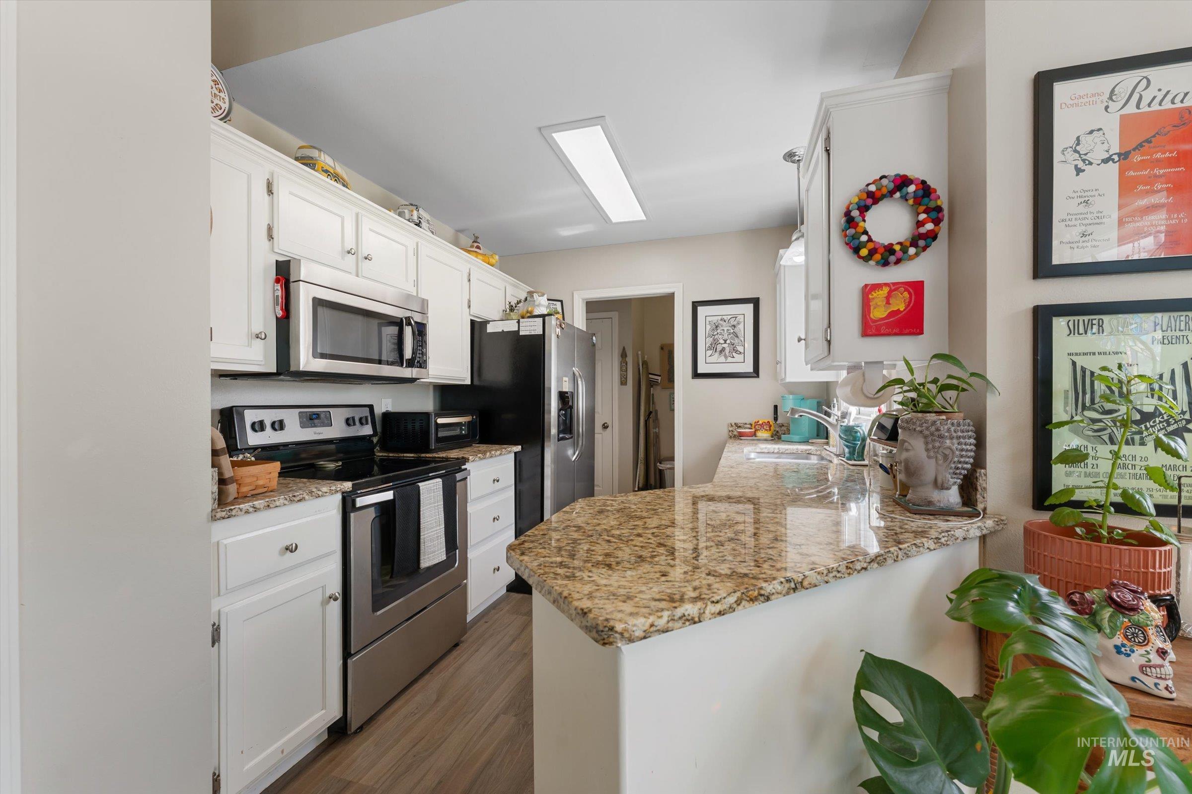 Kitchen with appliances with stainless steel finishes, white cabinetry, light stone countertops, and dark wood finished floors