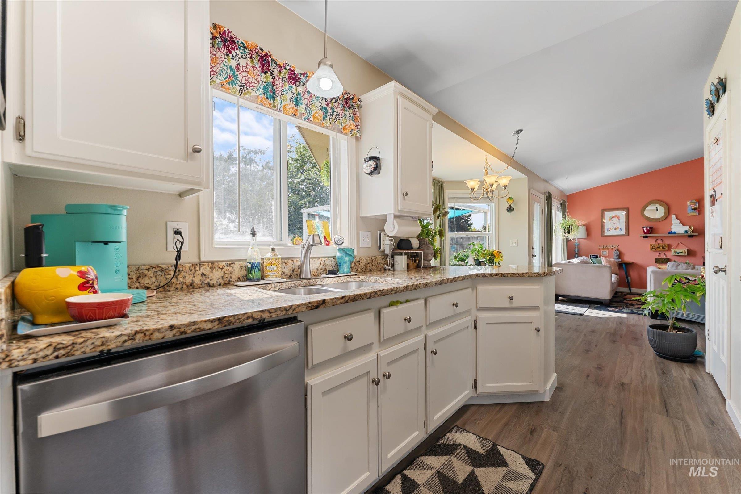 Kitchen featuring white cabinetry, stainless steel dishwasher, dark wood-type flooring, vaulted ceiling, and pendant lighting